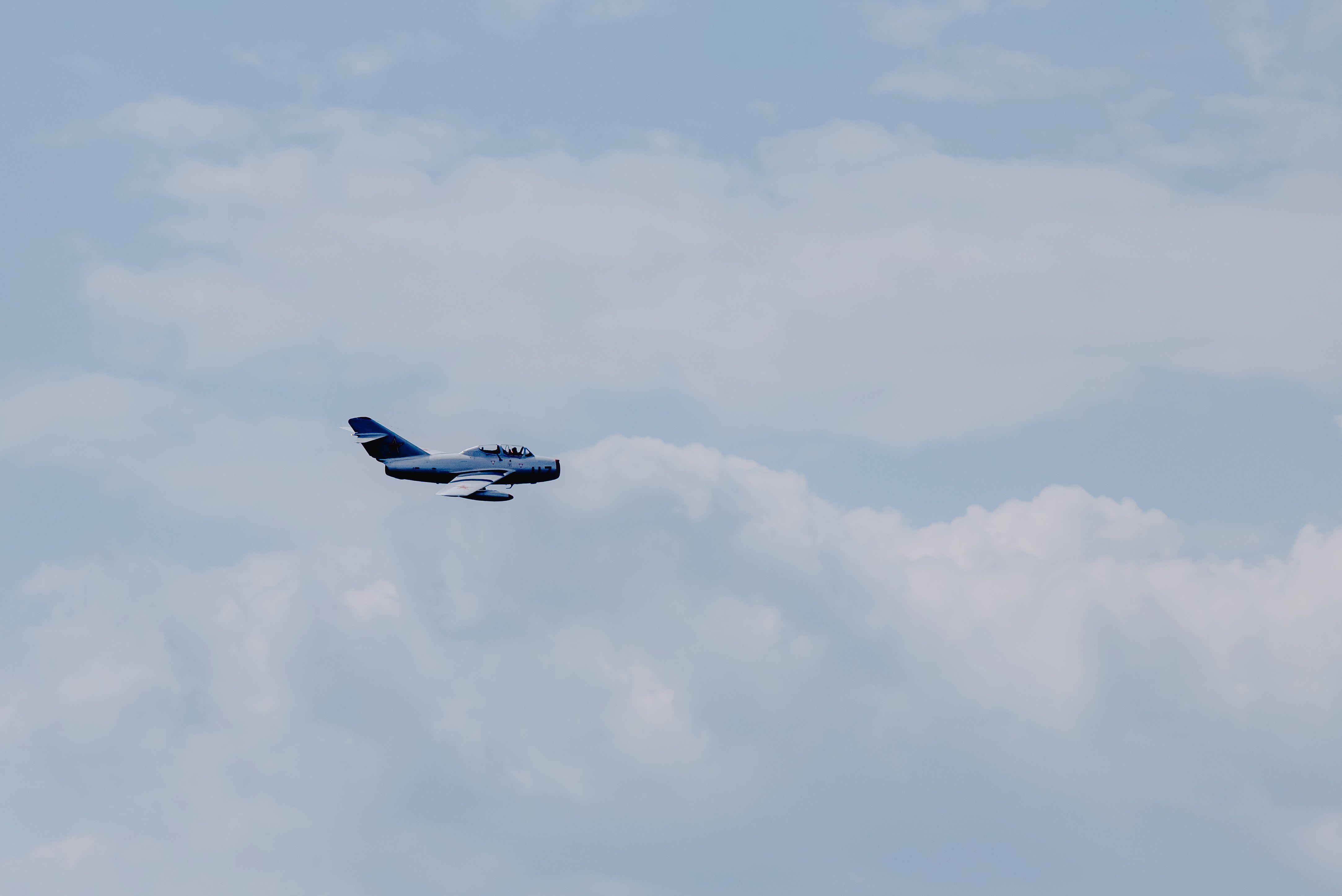 Creative design of modern fighter aircraft flying in light sky with fluffy clouds in daylight