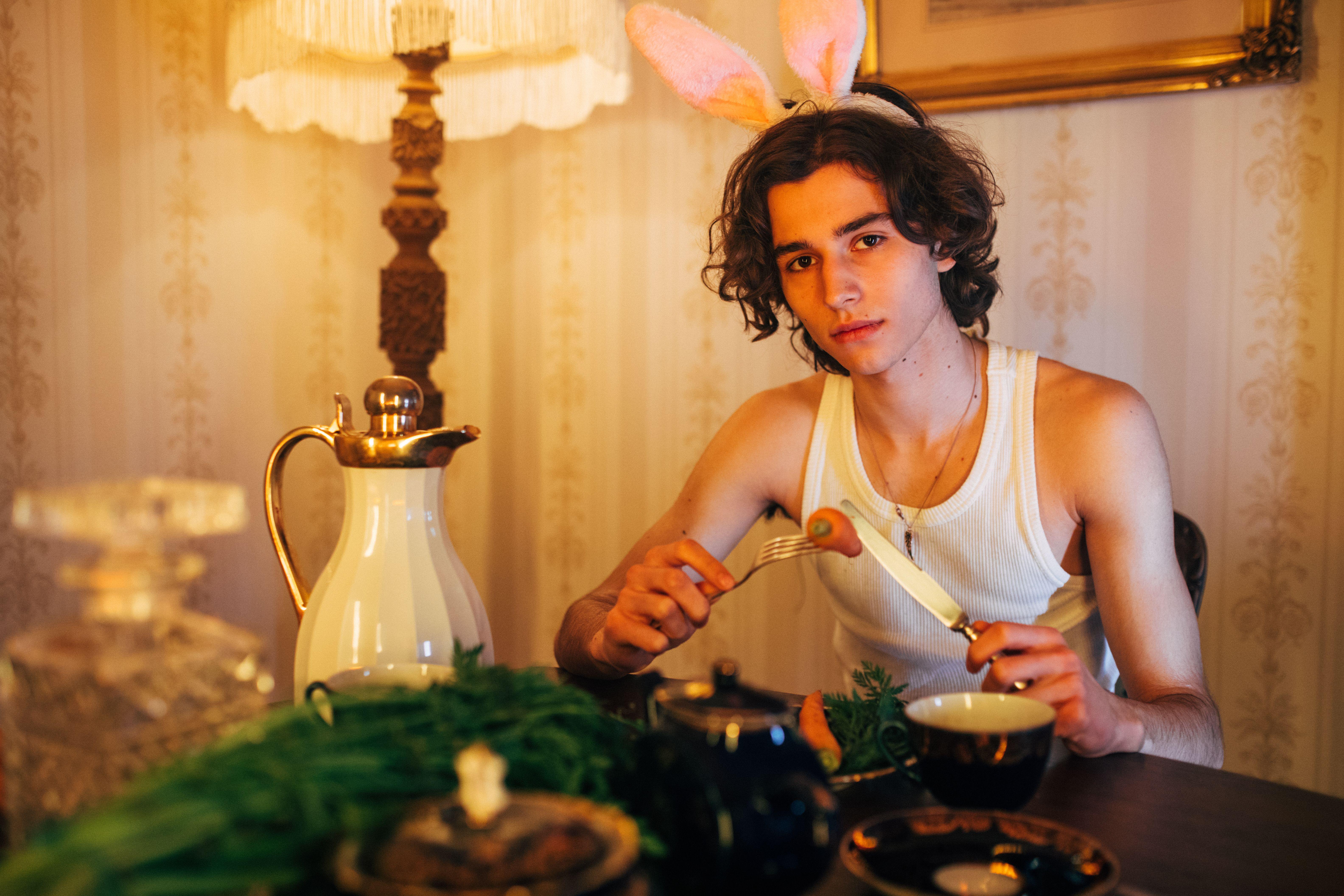 A young man wearing bunny ears enjoys a meal in a warmly lit, elegantly decorated setting.