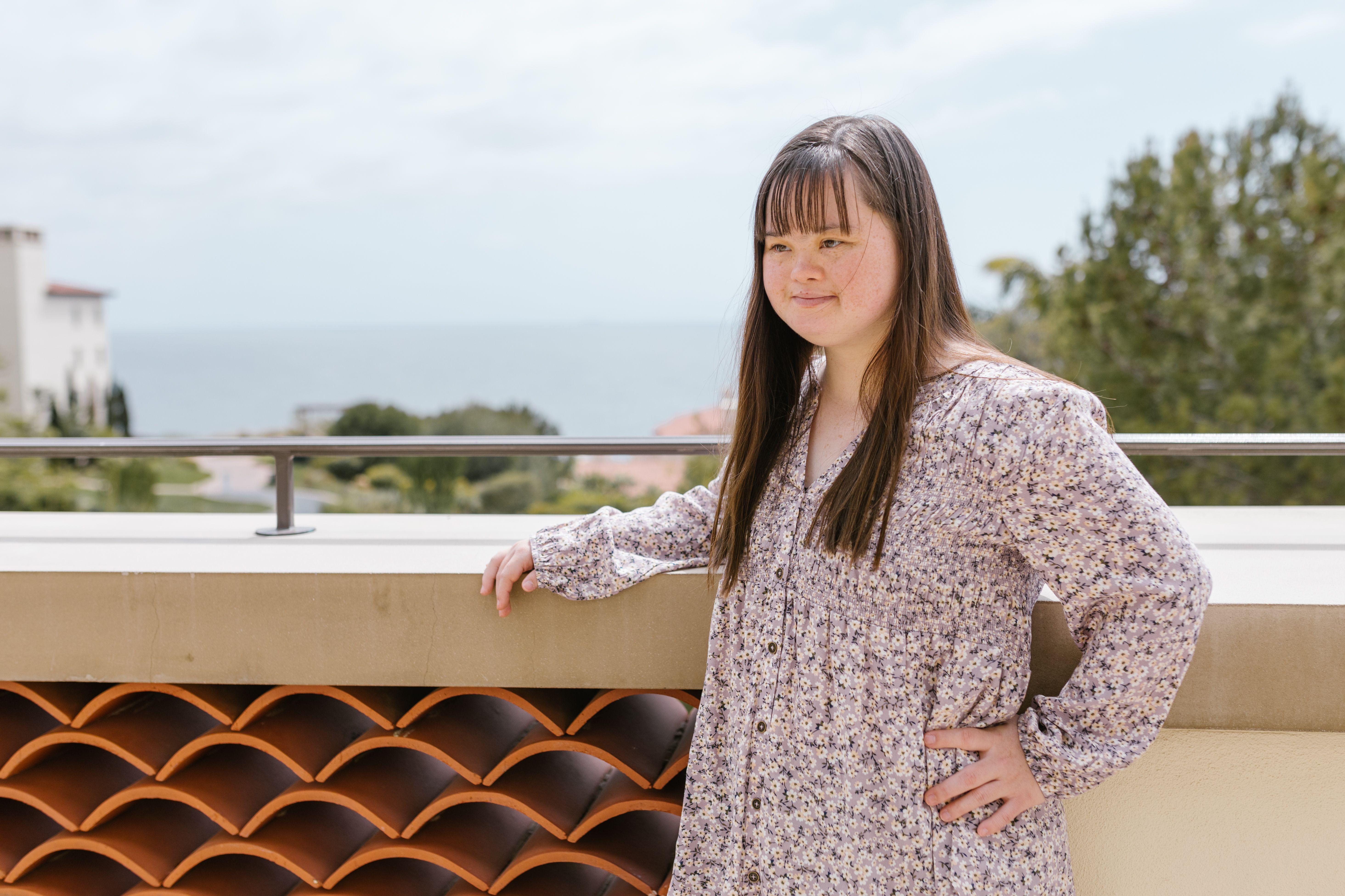 A young woman in a floral top stands outdoors, enjoying a scenic seaside view.