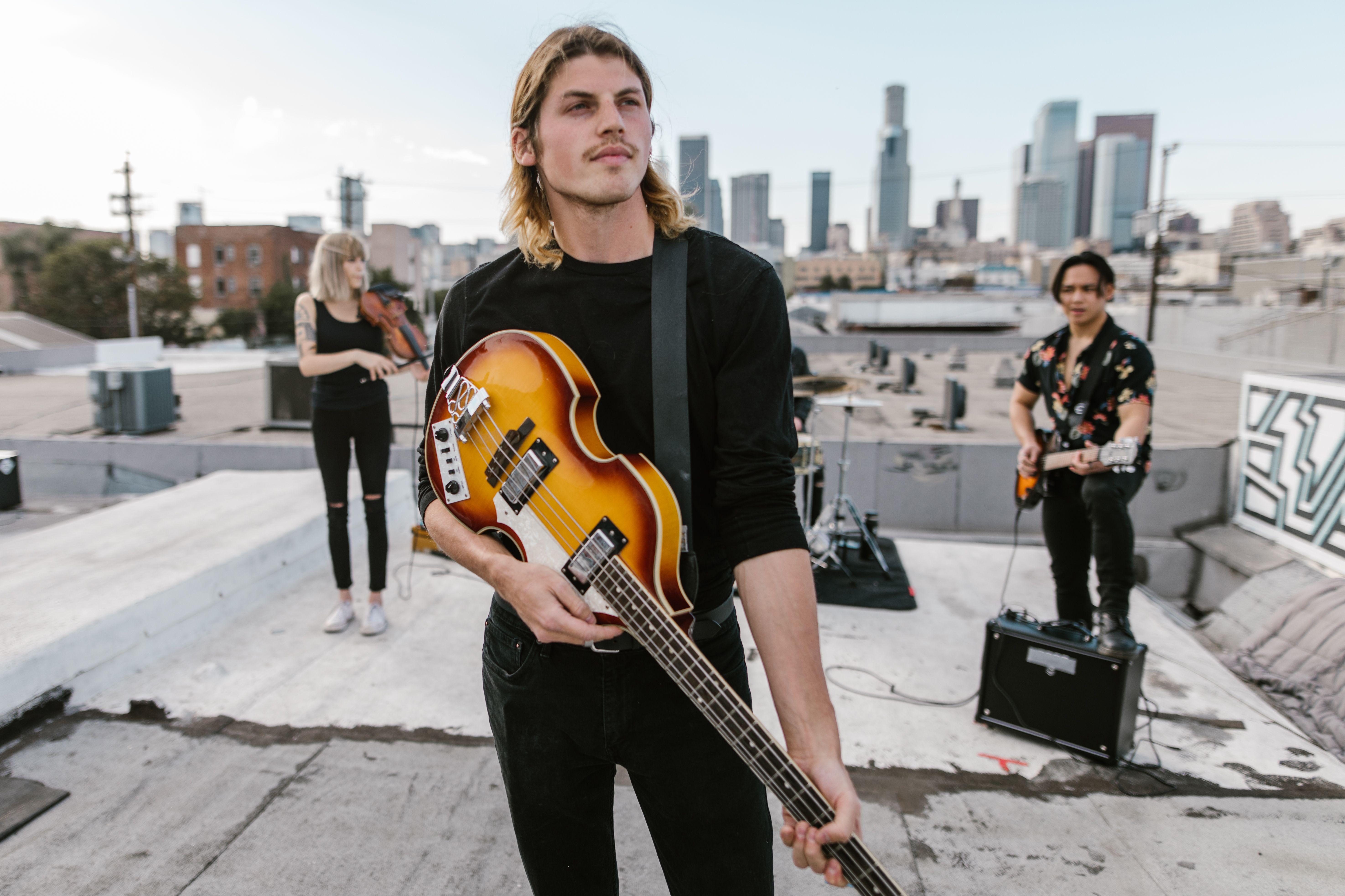 Musicians playing guitar and violin on a rooftop with city skyline backdrop.