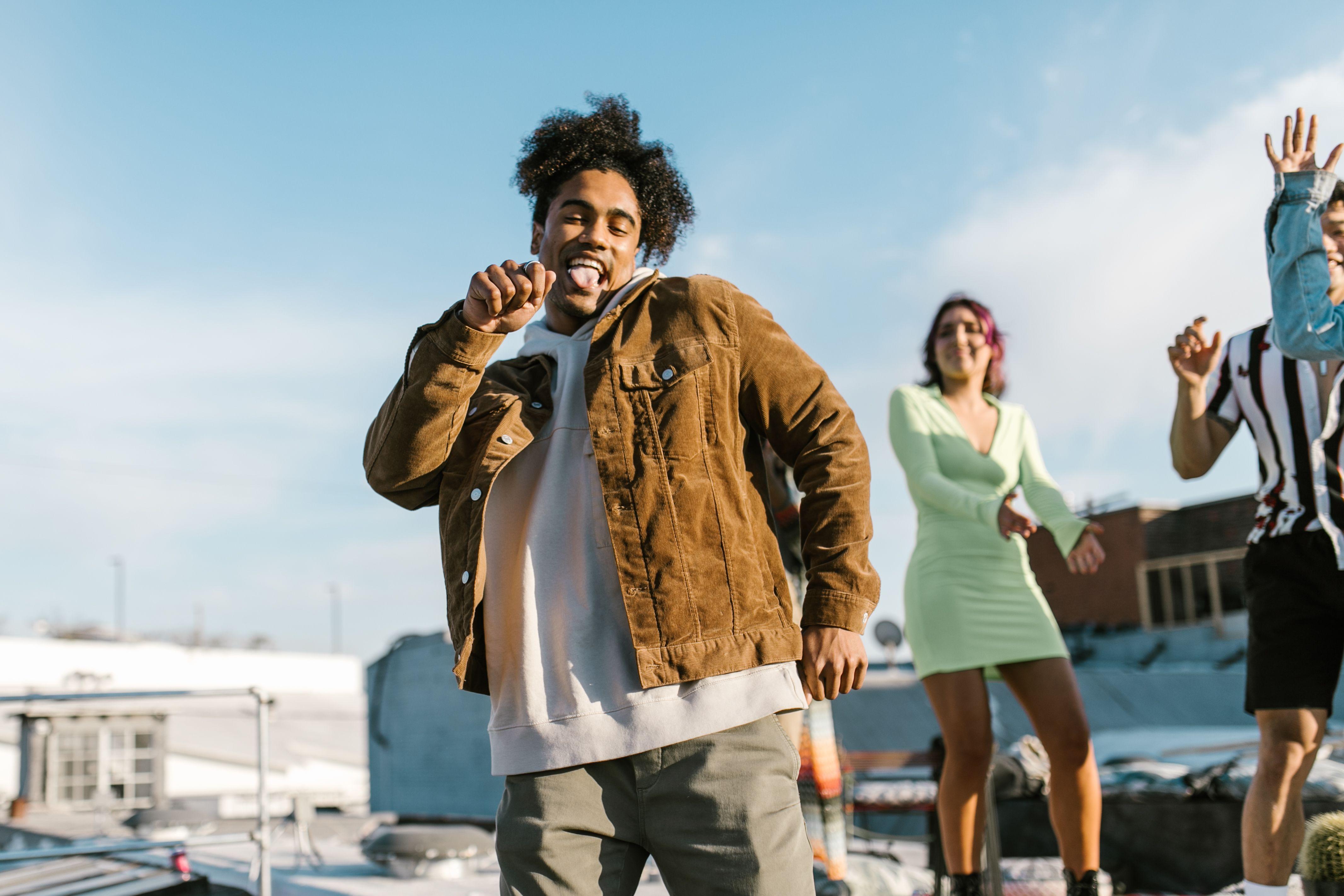 Group of friends dancing cheerfully on a rooftop, enjoying a sunny day together.