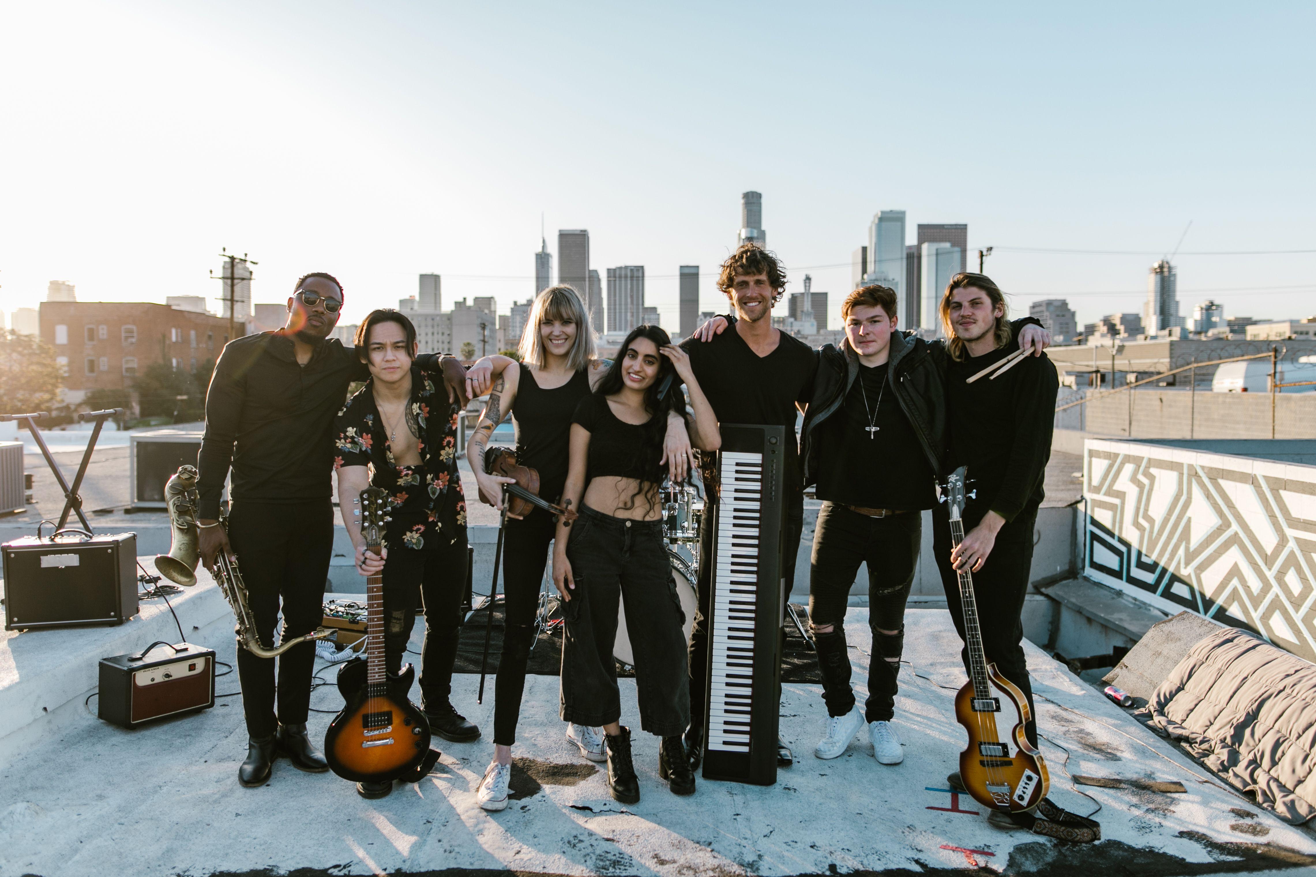 A diverse music band performing on a rooftop with a city skyline backdrop during sunset.