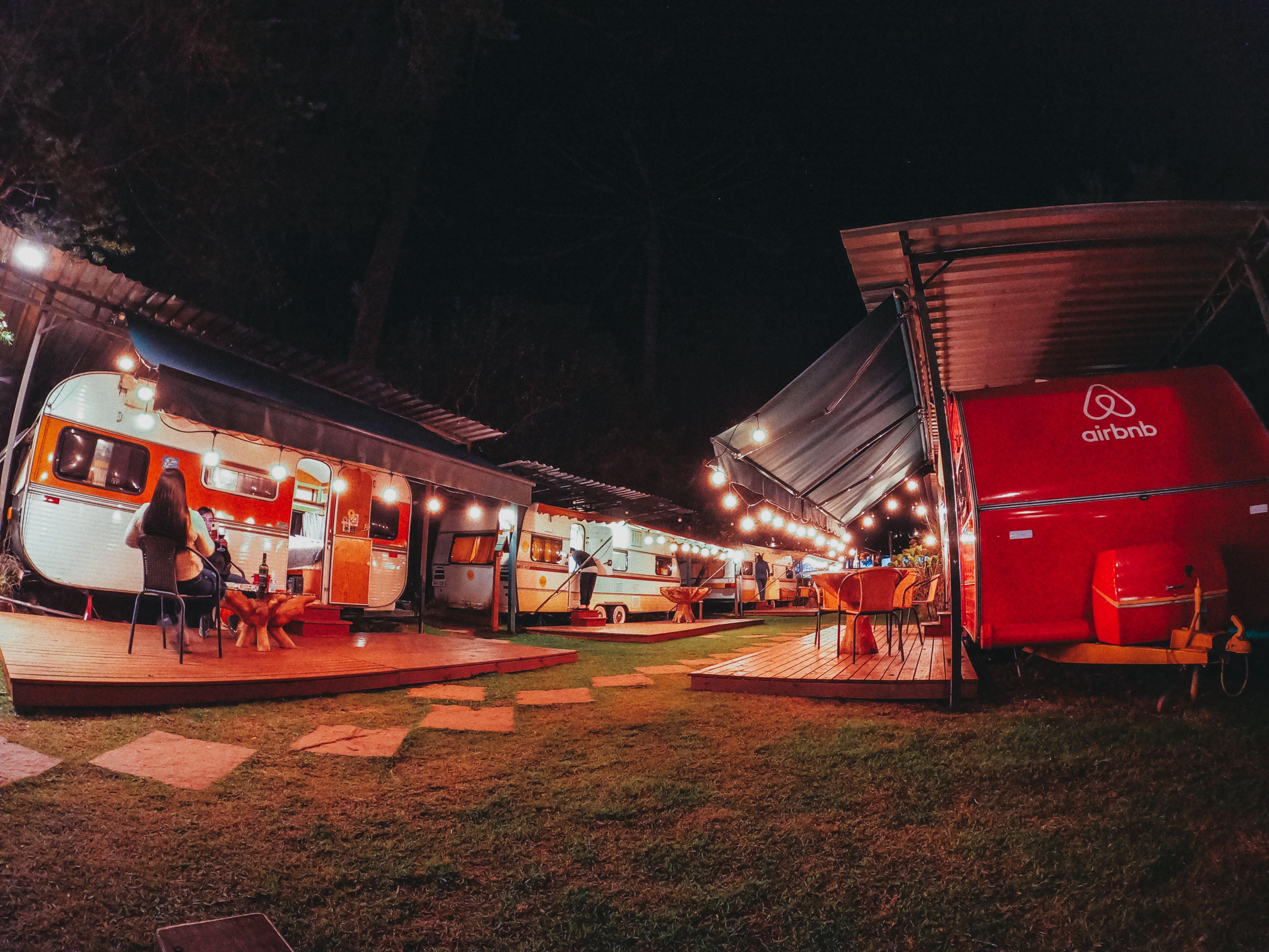 Travelers having picnic near caravan located at camping area among tall trees at night