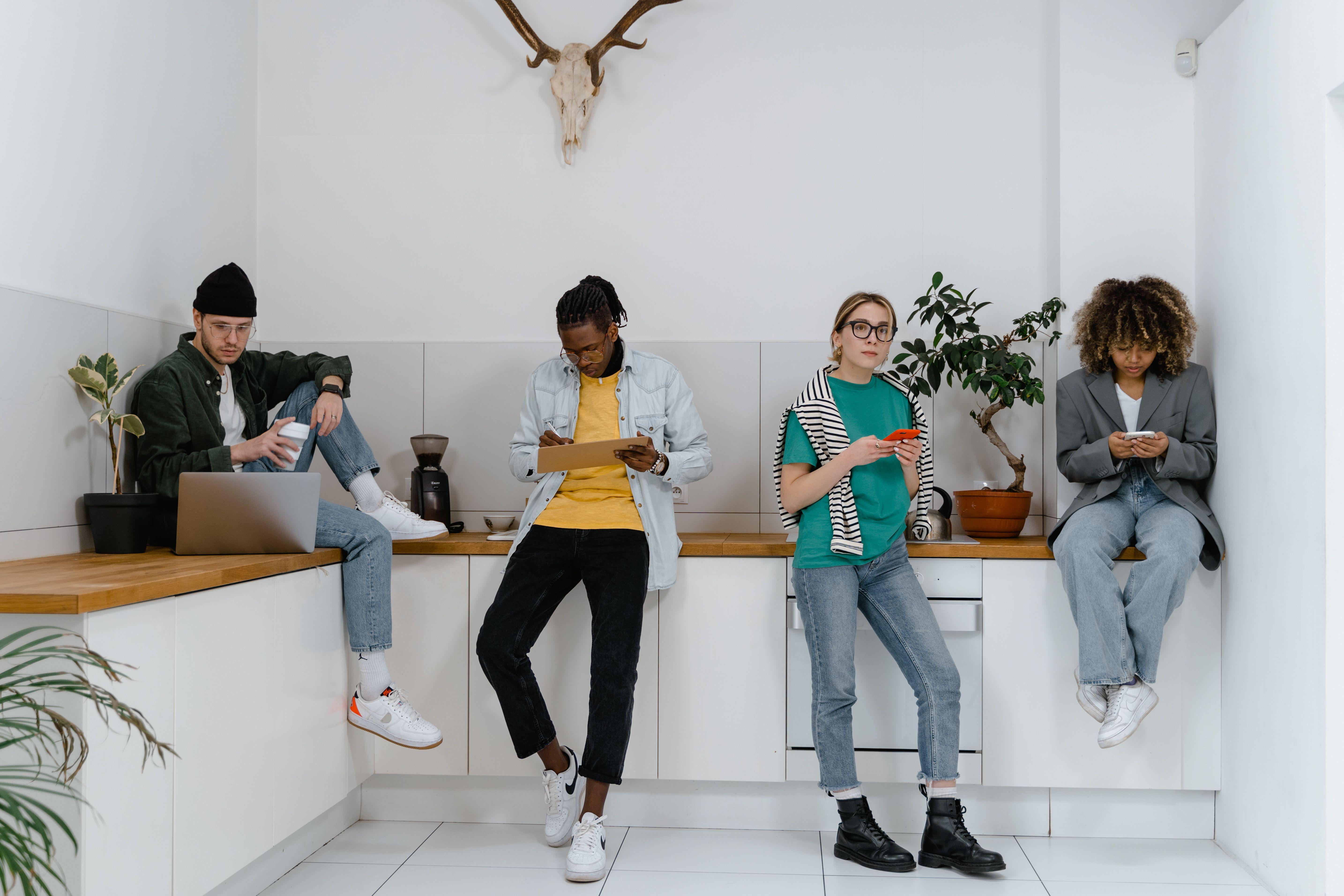 Casual and diverse colleagues using gadgets in a modern office kitchen area.