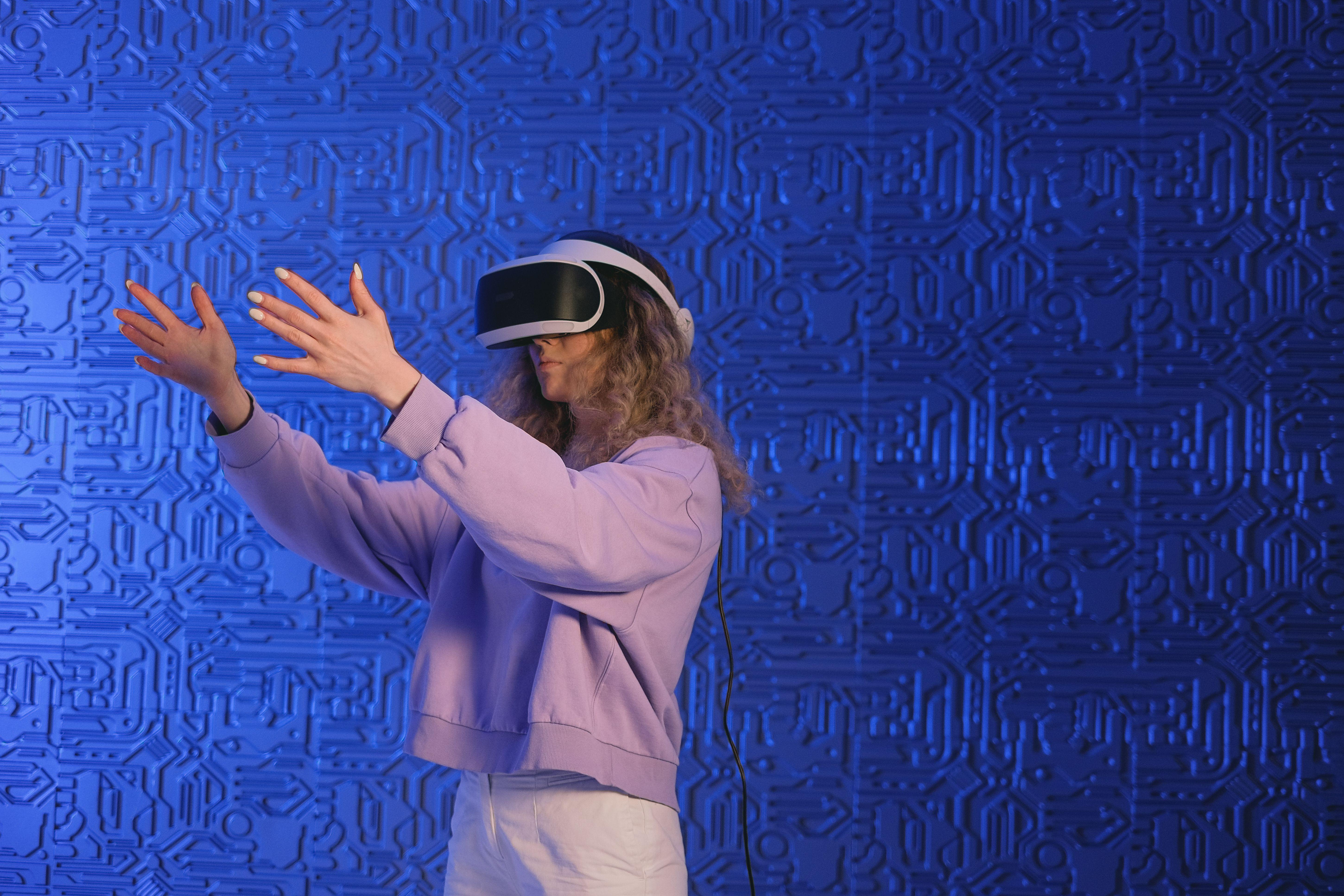 Adult woman with VR goggles interacting in a virtual environment against a blue background.