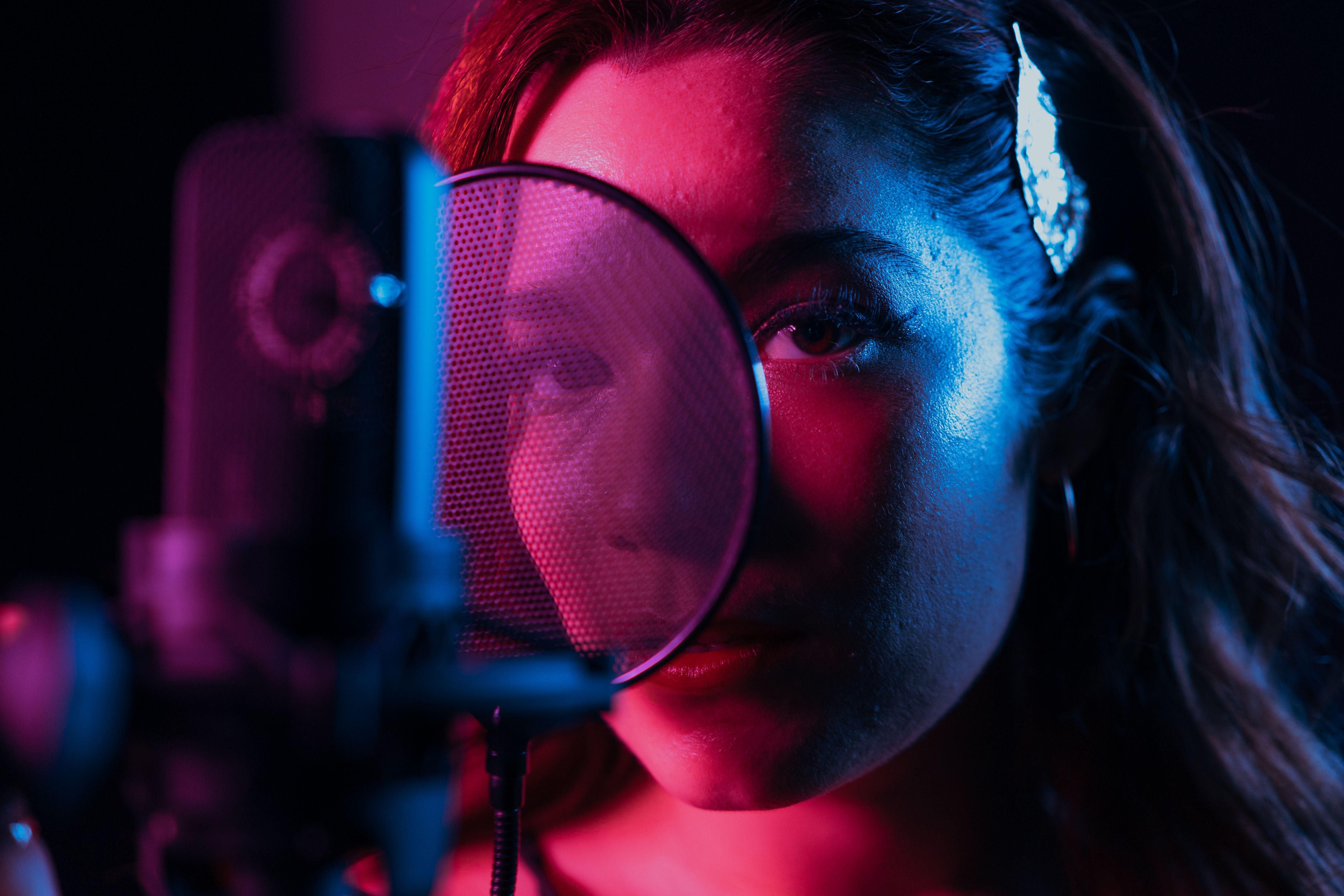 A close-up of a female singer in a recording studio with vibrant lighting and a condenser microphone.