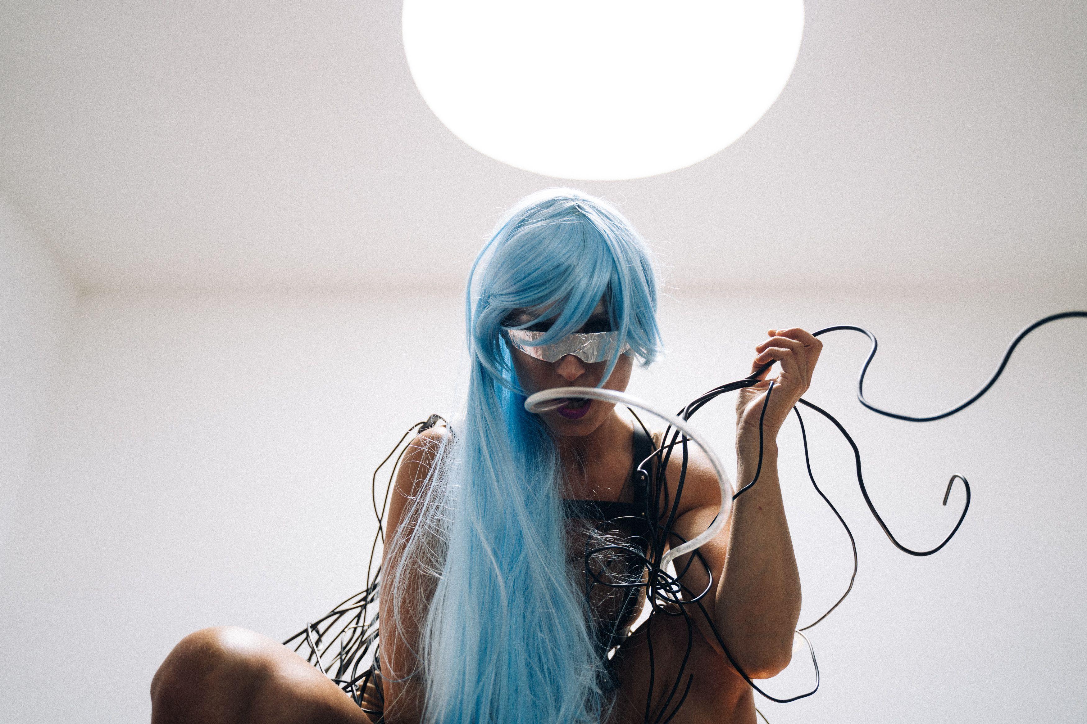 A woman in a cyberpunk outfit with blue hair and wires, embodying a futuristic concept.