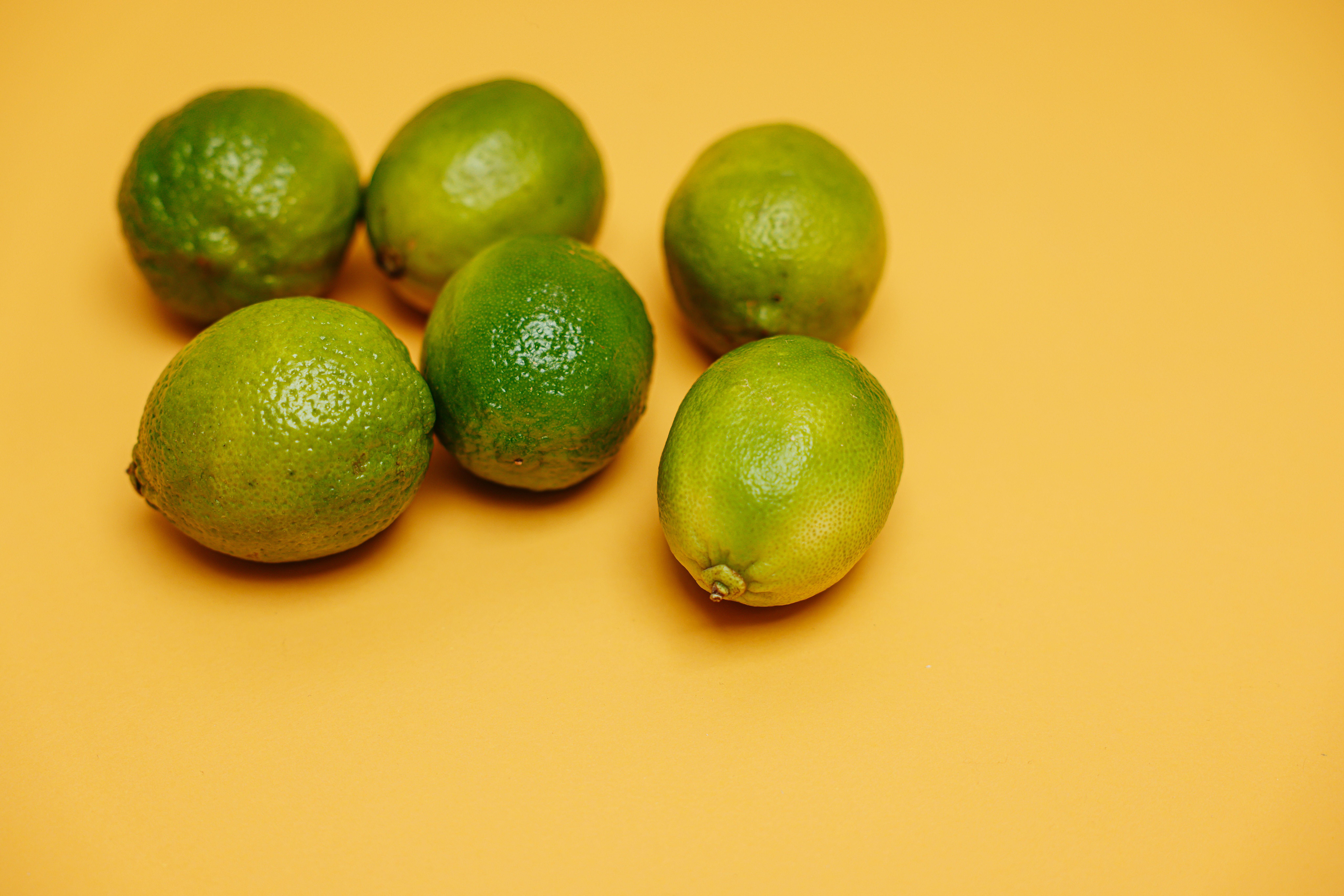 Six fresh green limes arranged on a vibrant yellow background, emphasizing freshness and citrus zest.