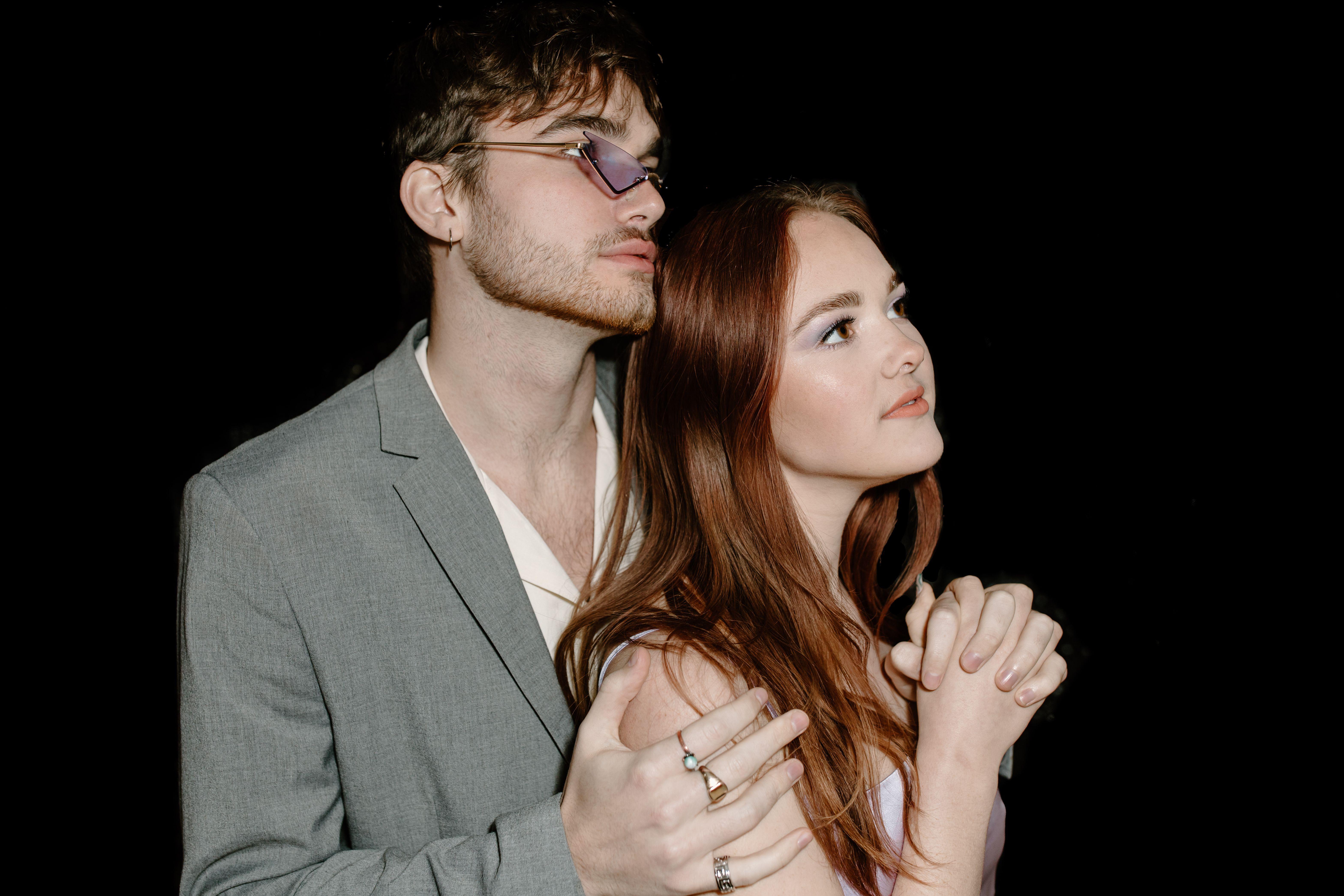 Stylish couple in gray suit and dress embracing under a black backdrop.