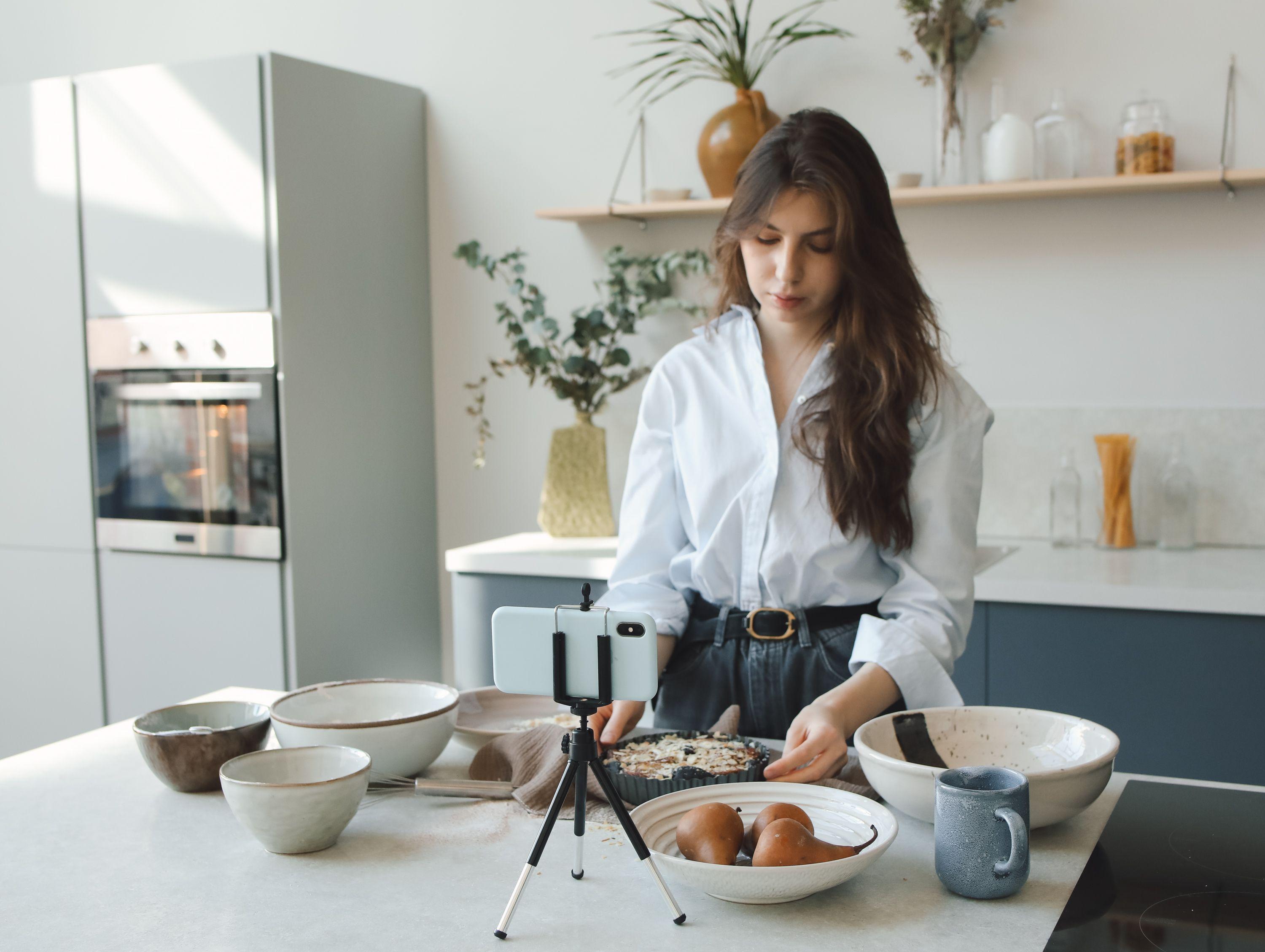 A woman cooking in a stylish kitchen while recording a vlog.