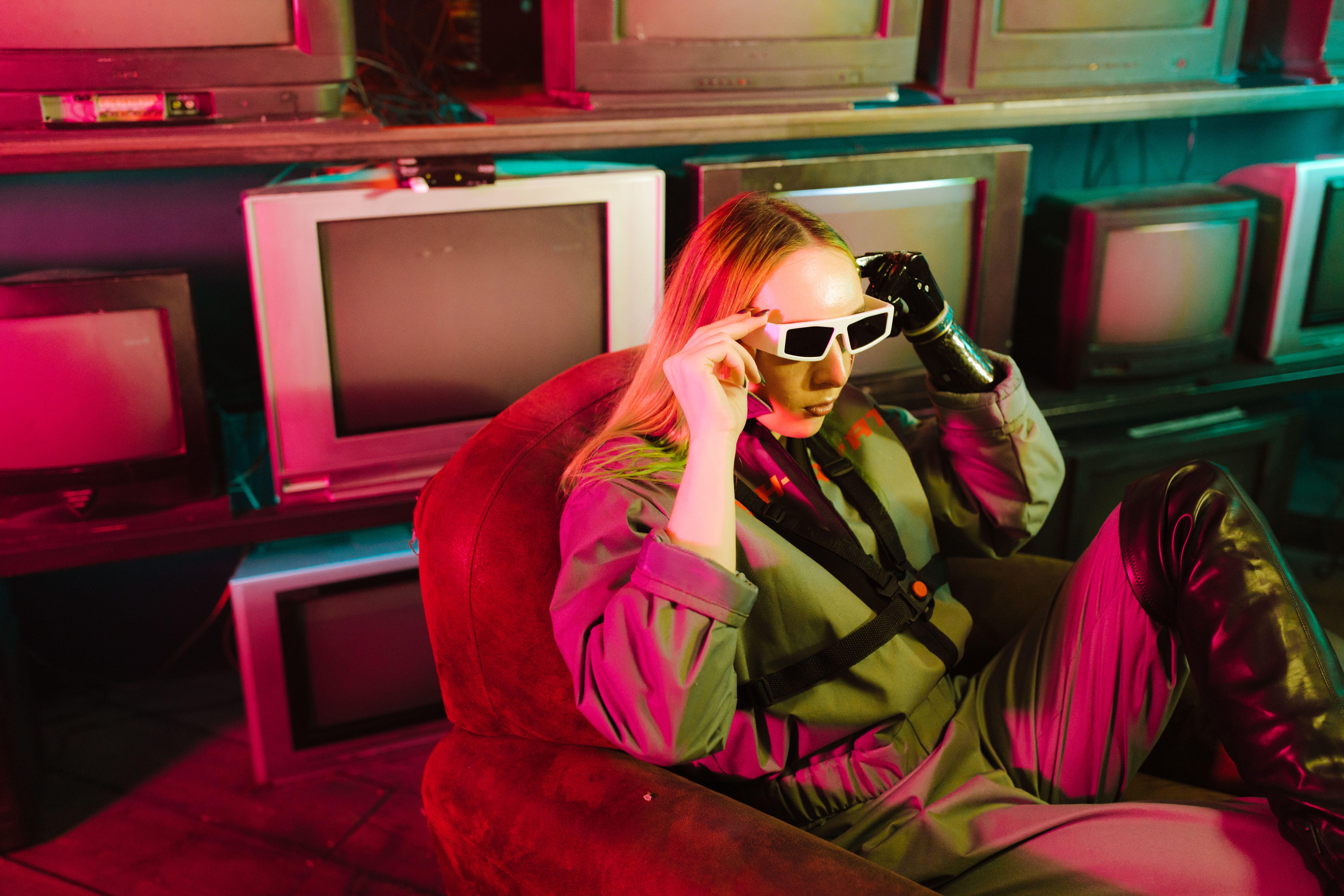 A woman in futuristic attire poses with vintage TVs under neon lights.