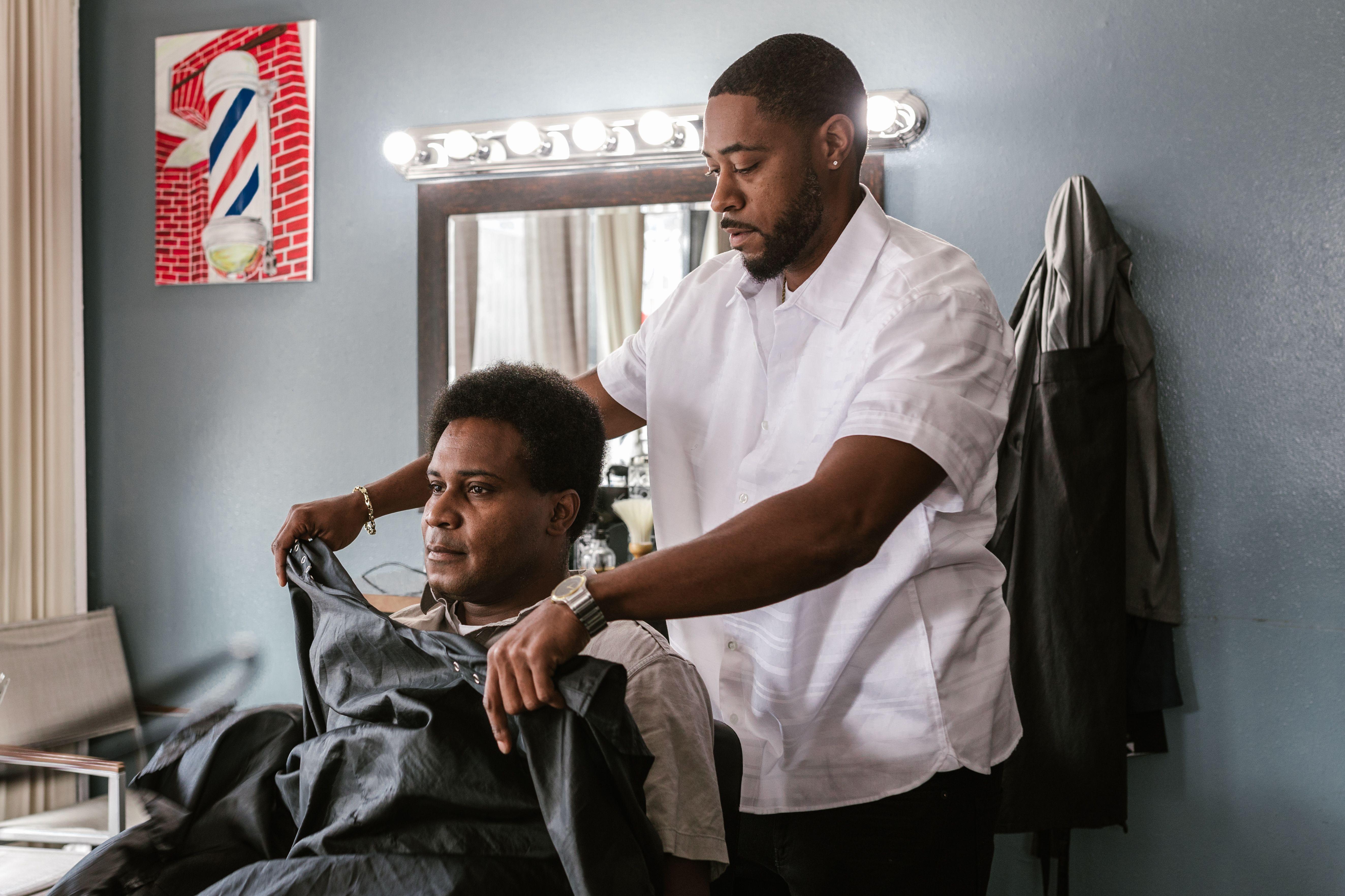 Professional barber drapes apron on client in stylish salon, preparing for a haircut session.
