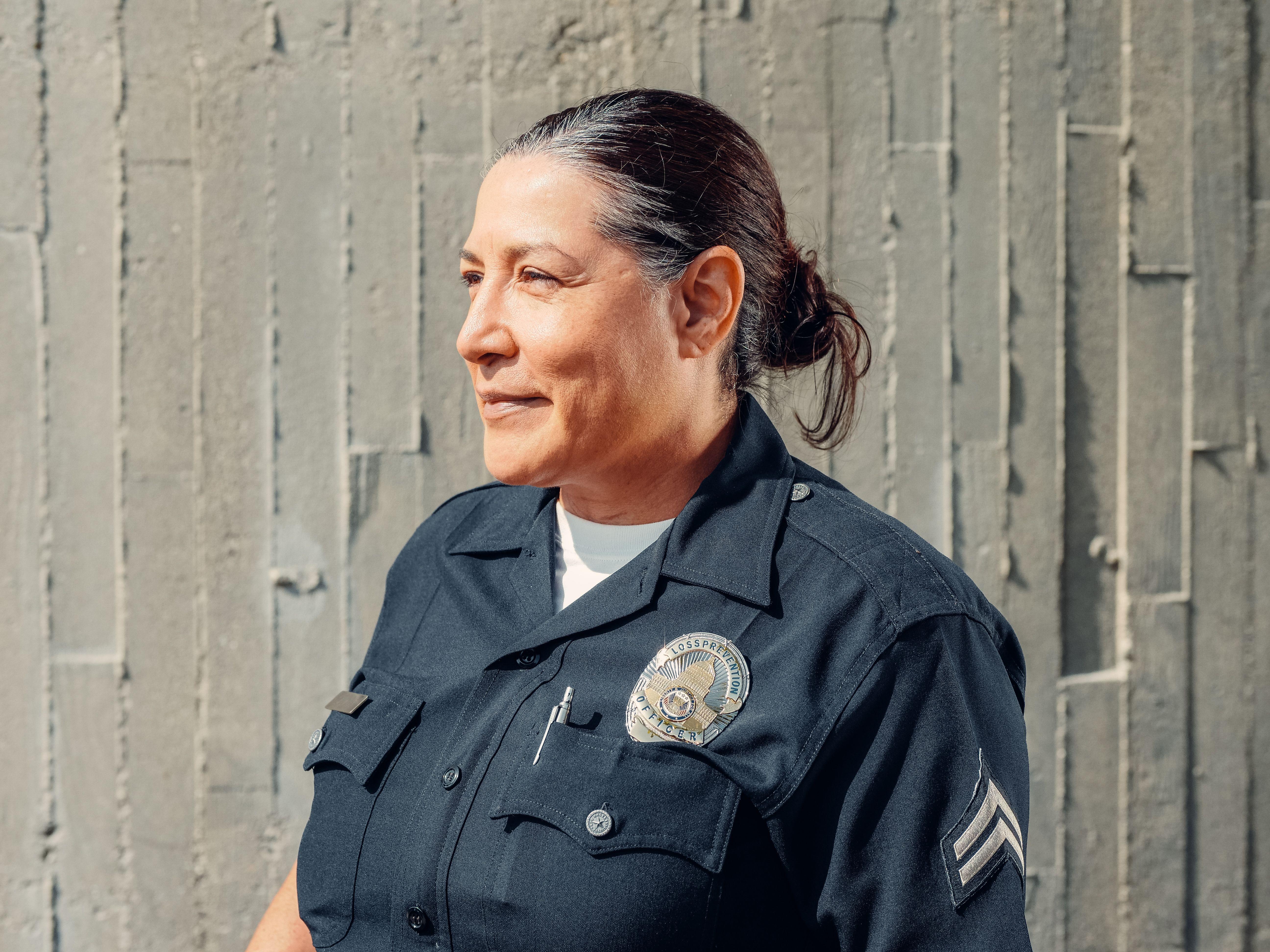 Portrait of a confident female police officer in uniform, standing outdoors against a textured wall.