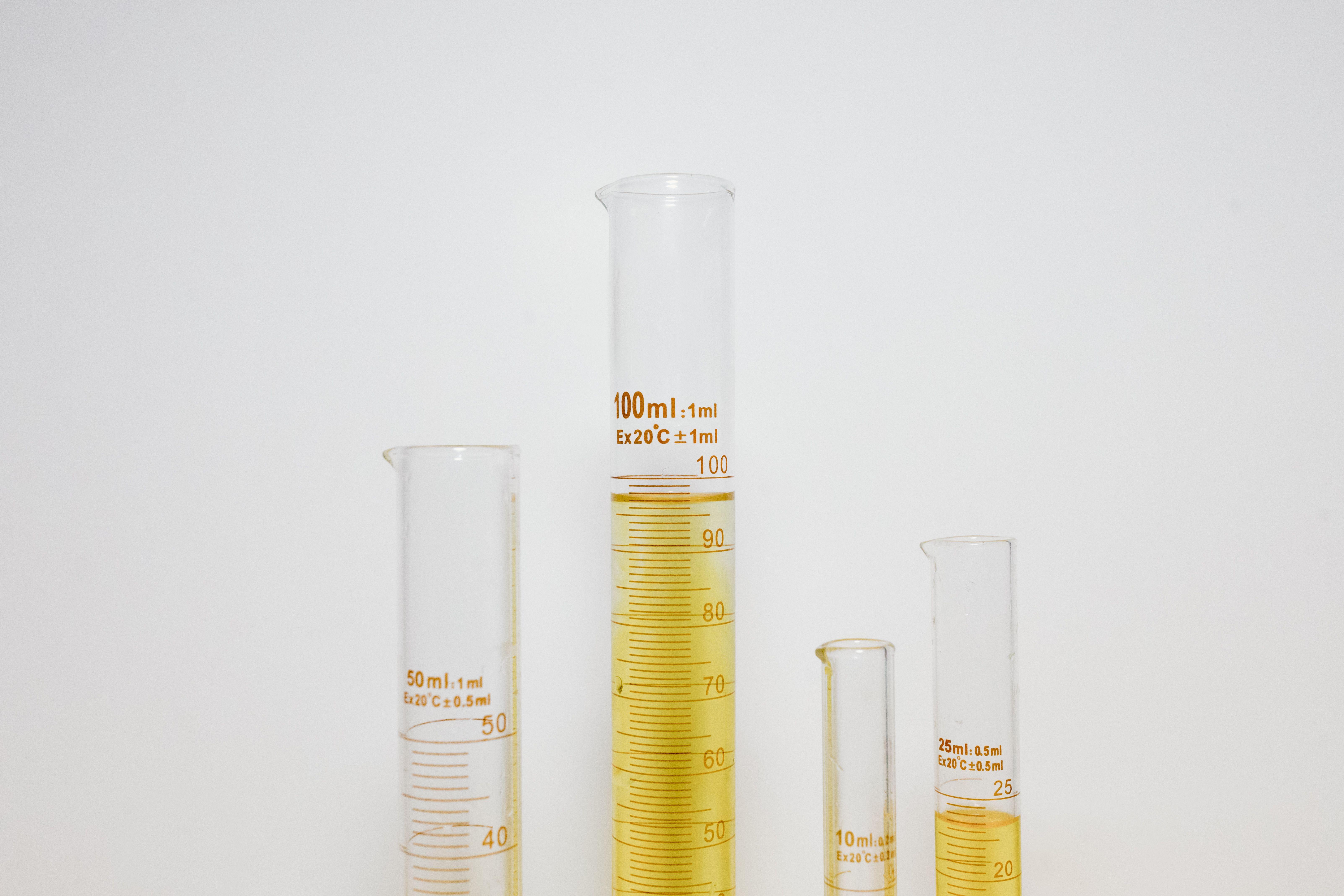 Close-up of graduated cylinders filled with yellow liquid in a laboratory setting.