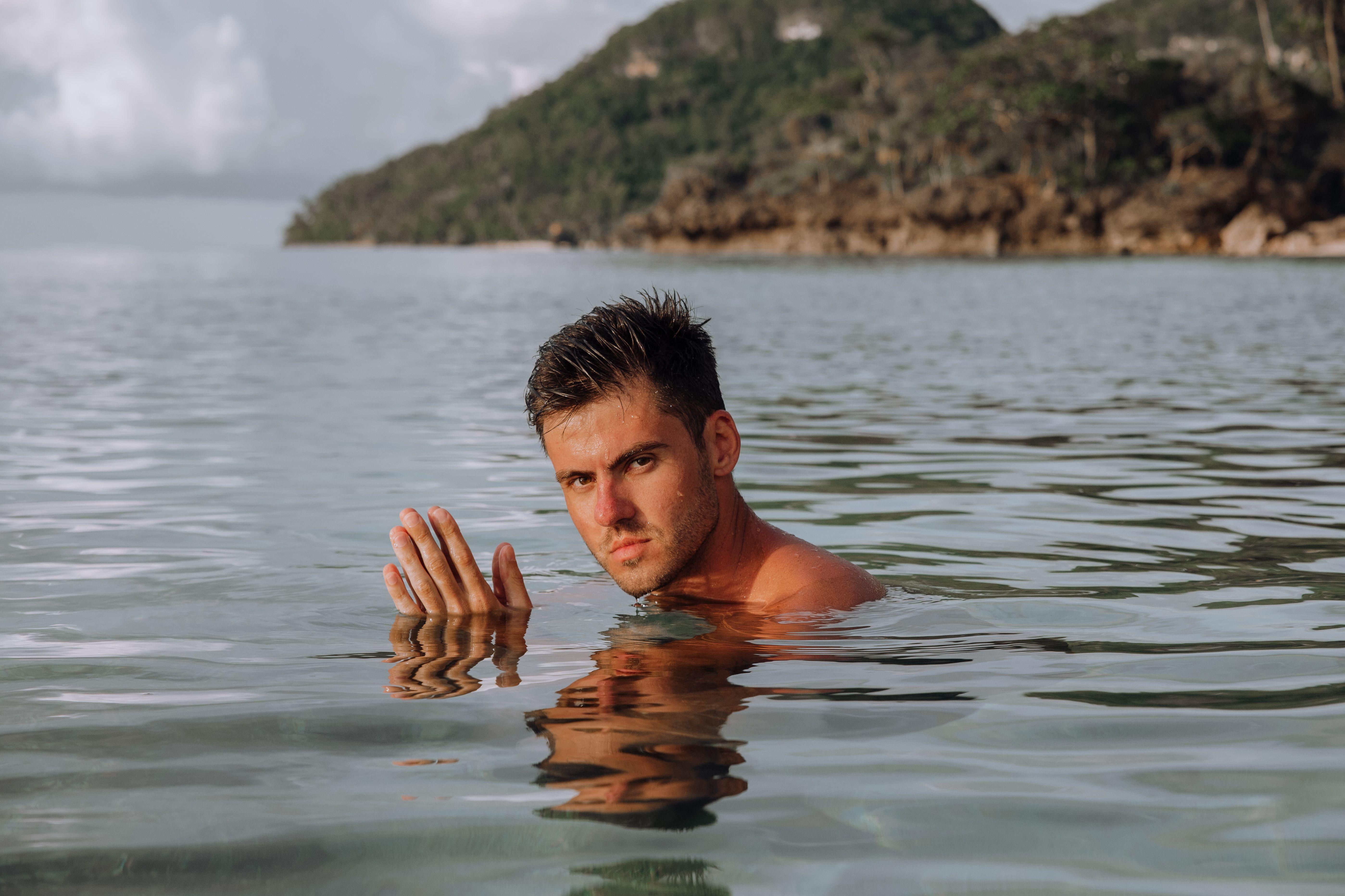 A young man enjoying a swim in clear tropical waters with lush green islands in the background.