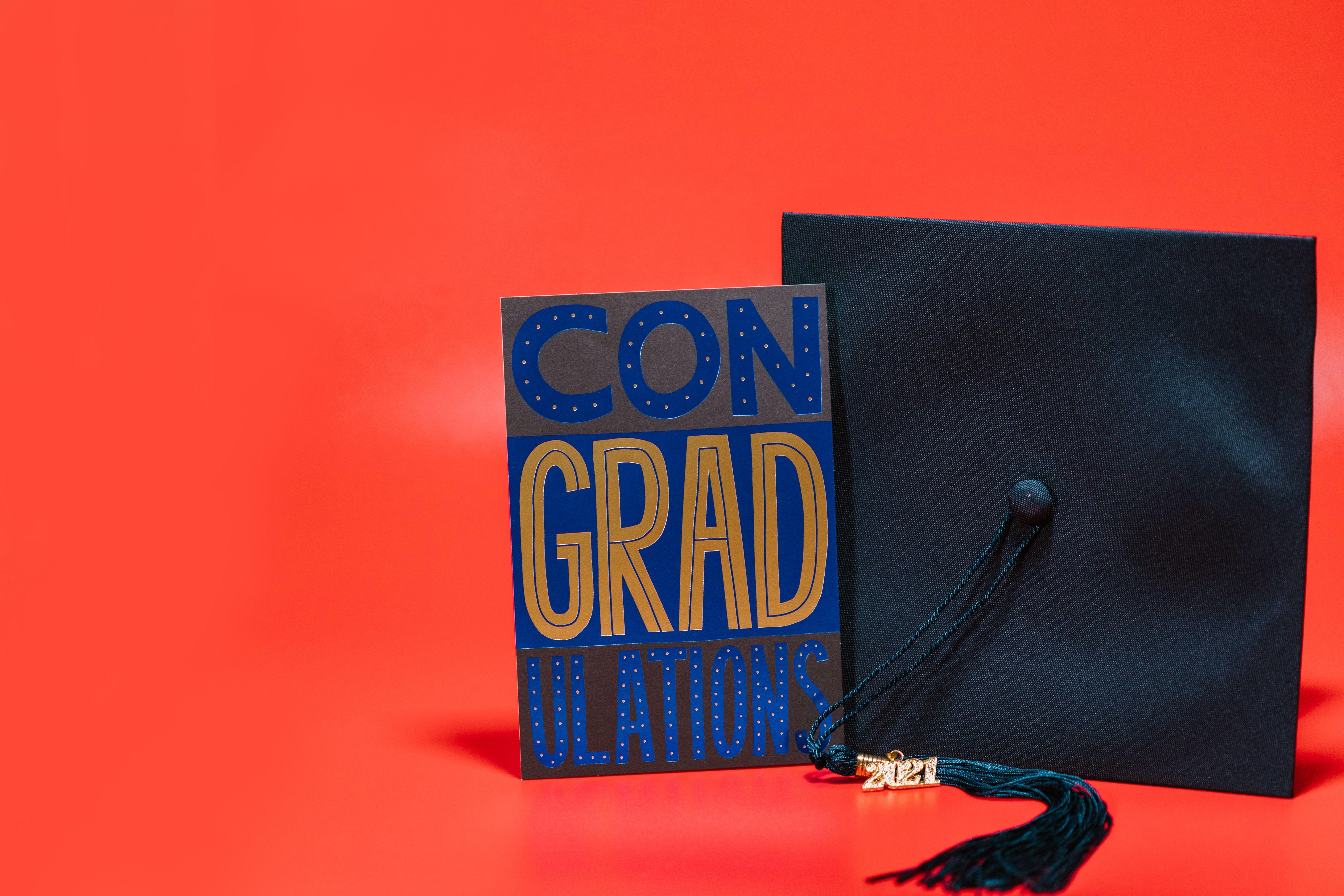 A stylish graduation card and cap on a vibrant red background, ideal for celebration themes.