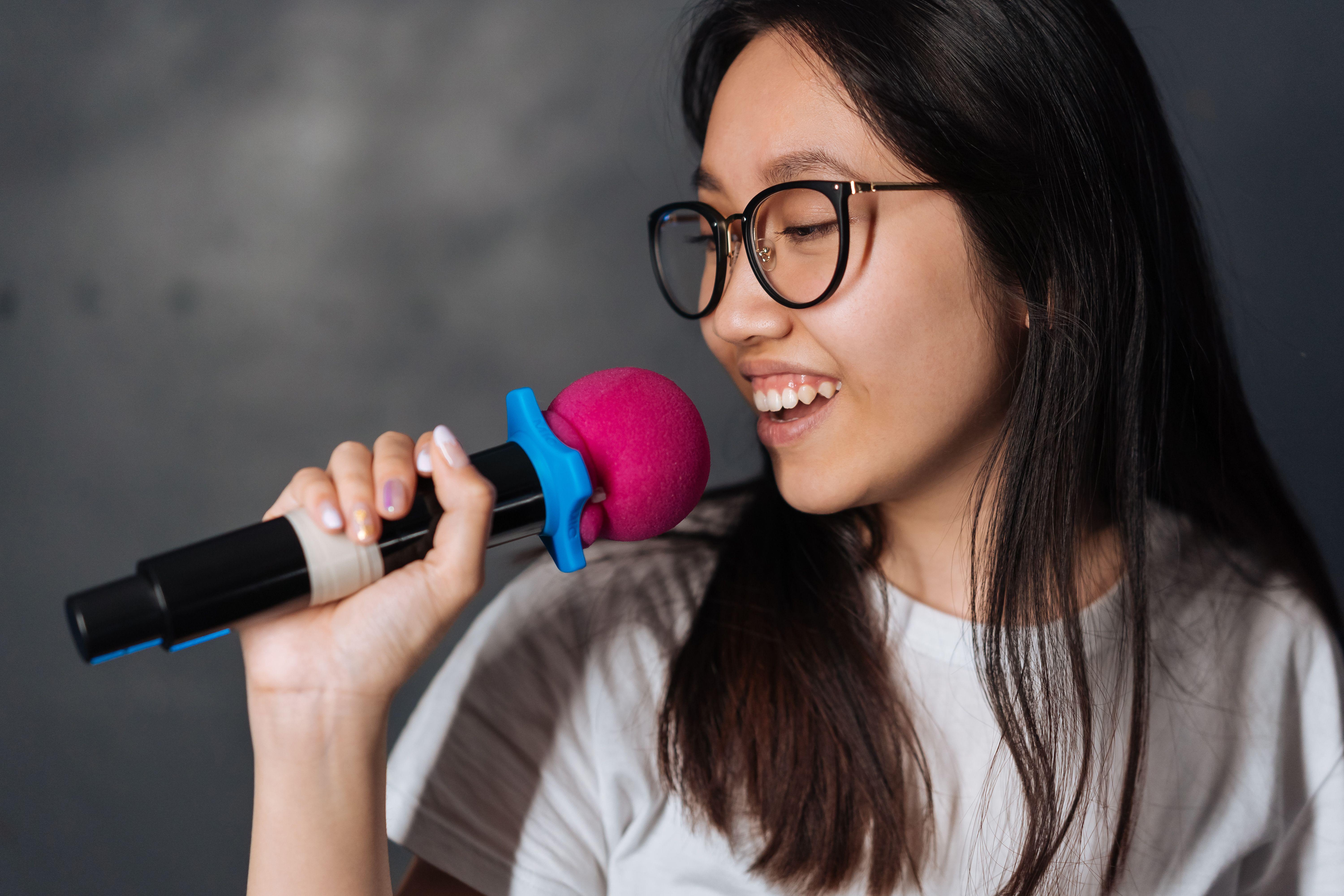 A young woman happily sings into a microphone during a karaoke session indoors.