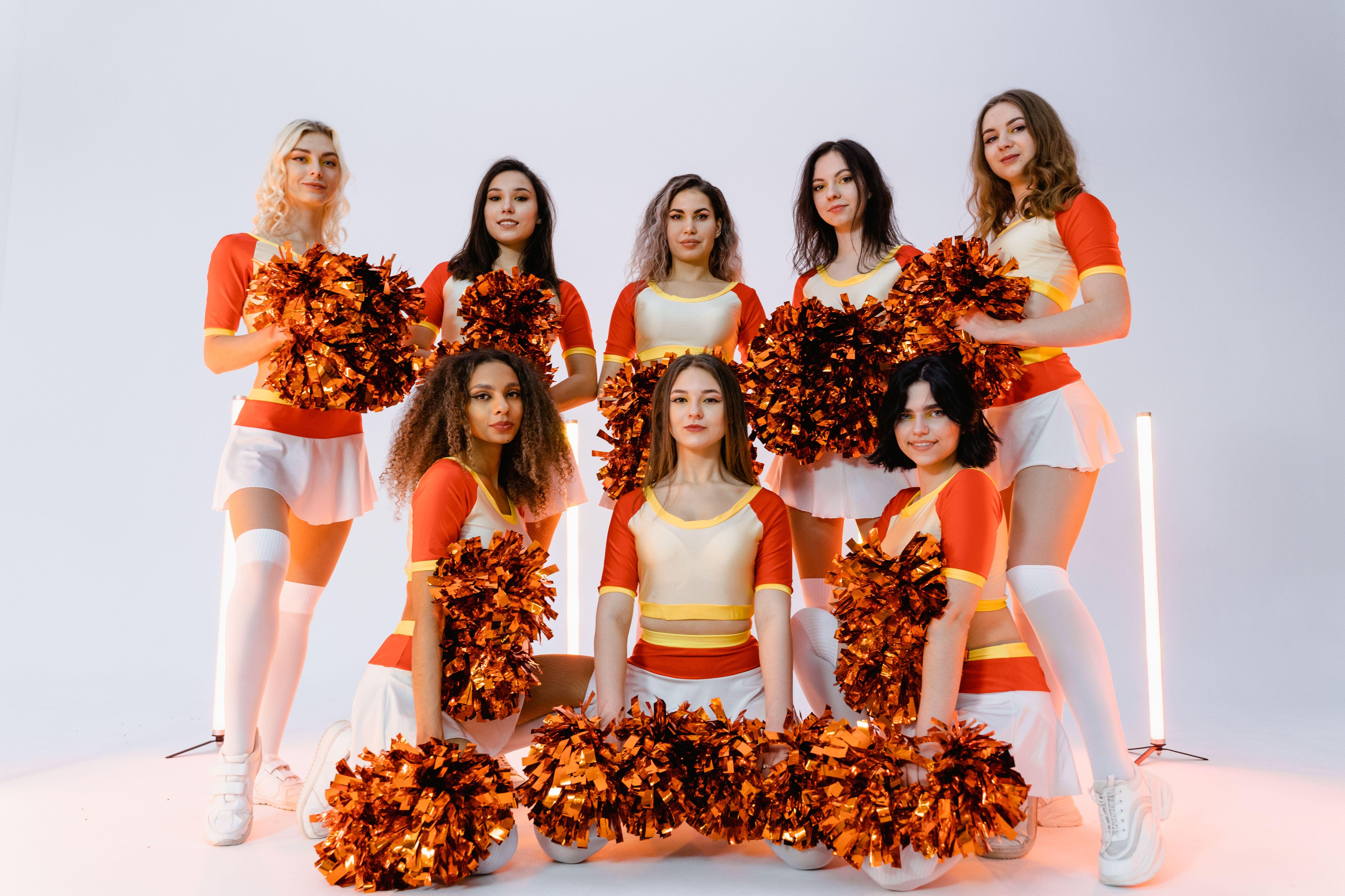 Group of diverse cheerleaders in vibrant uniforms posing with pompoms in a studio setting.