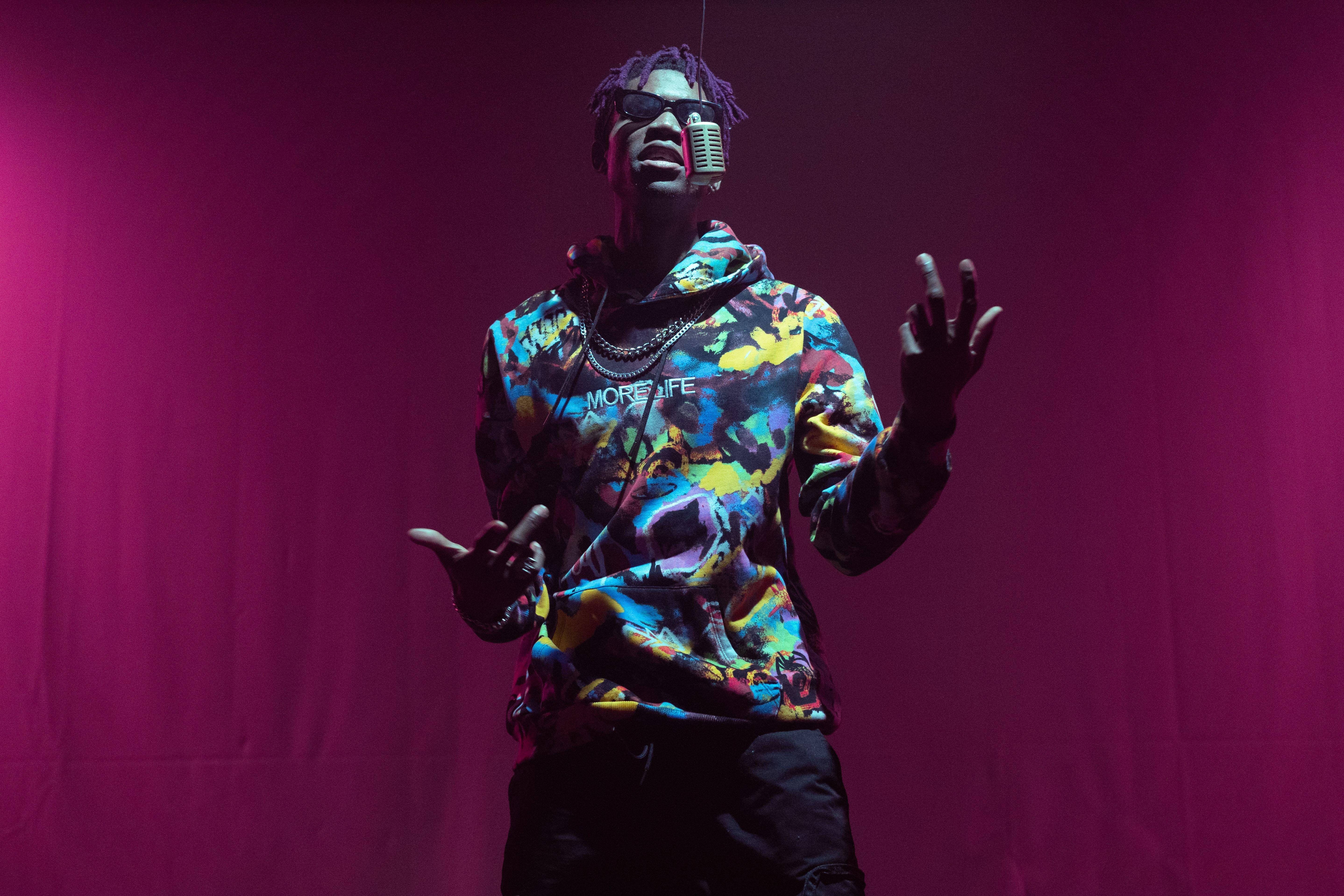 Rapper in colorful hoodie performing with mic on red stage. Captivating music and style.
