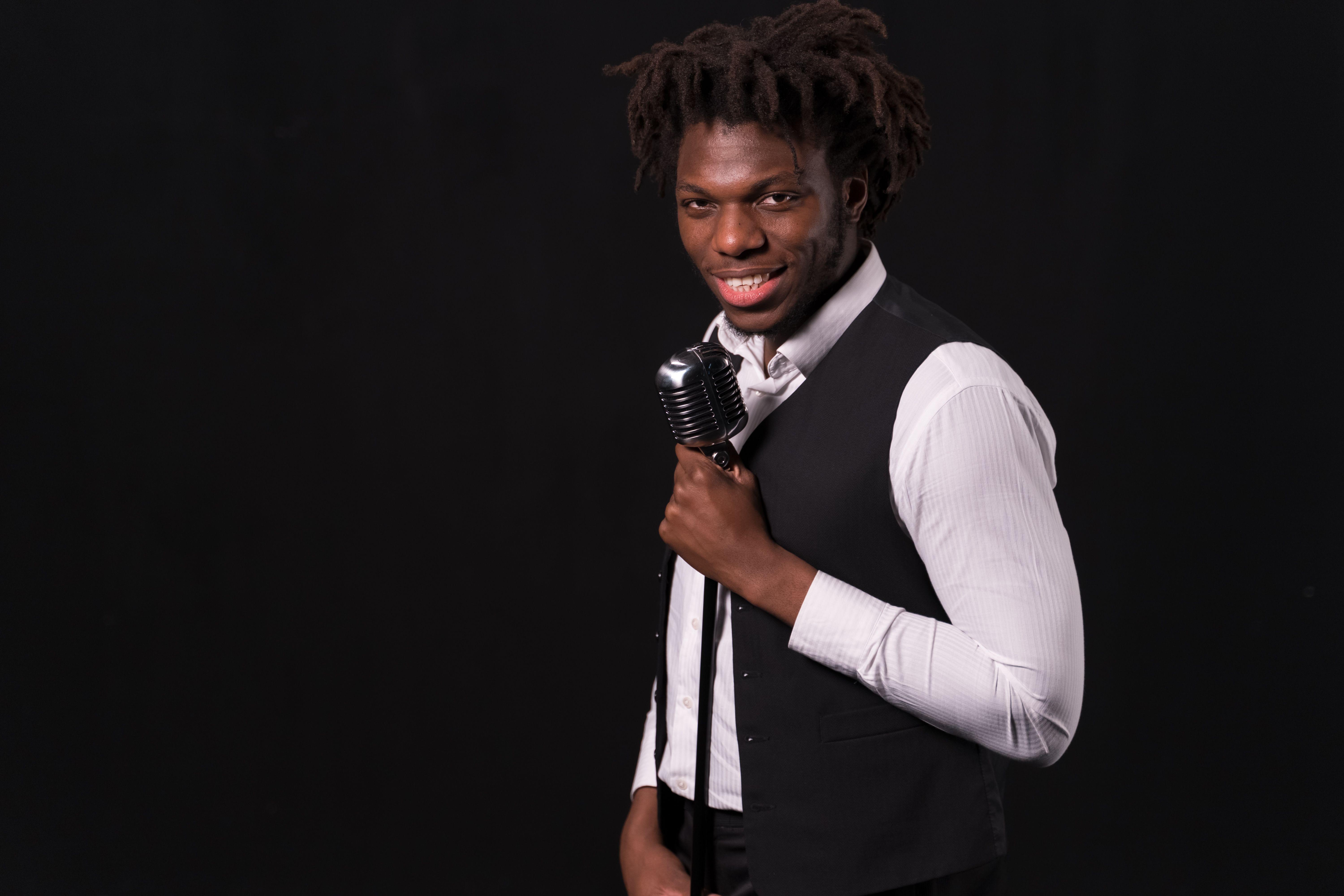 Smiling singer holding a vintage microphone against a black background.