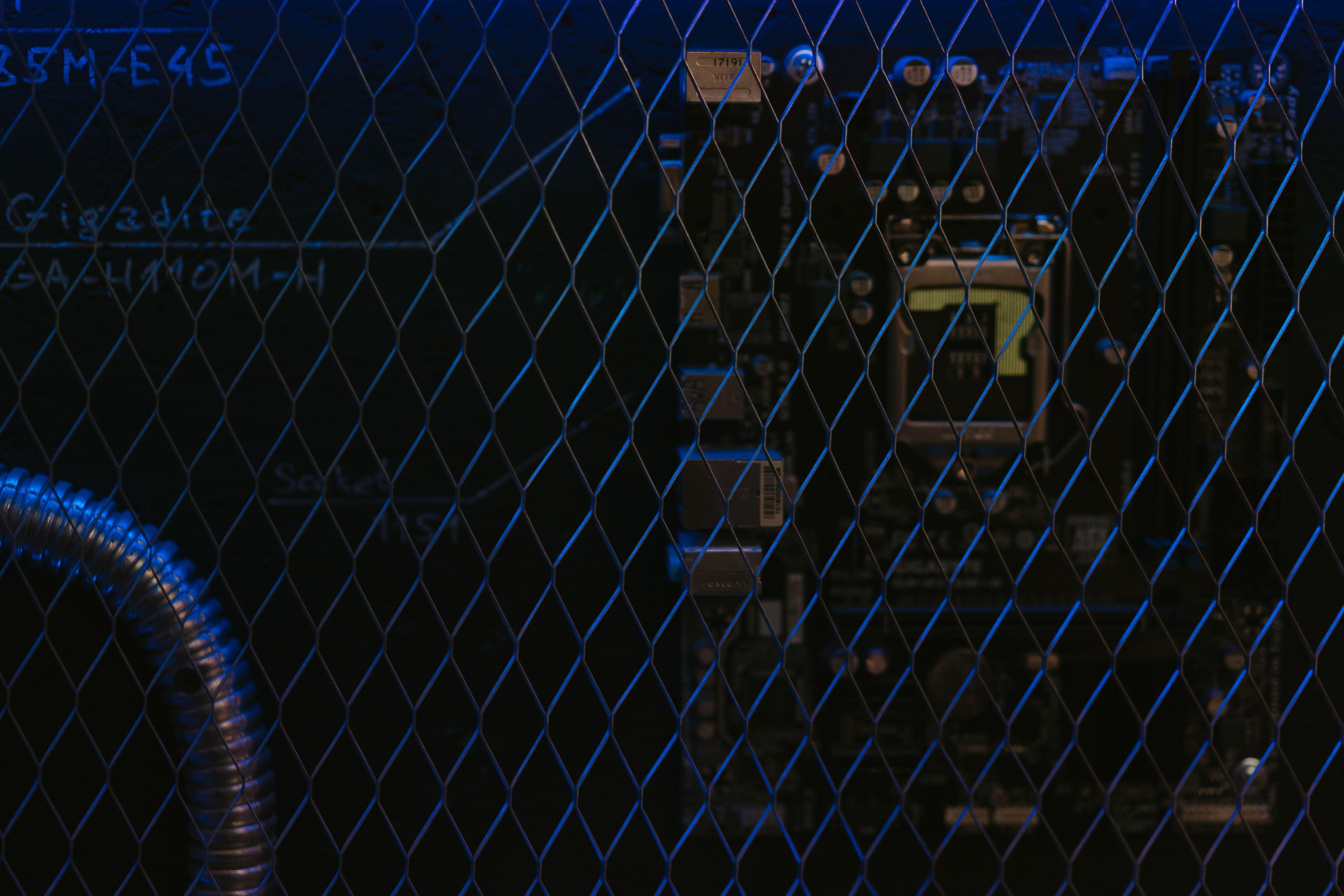 Artistic view of a circuit board through metal mesh with blue lighting.