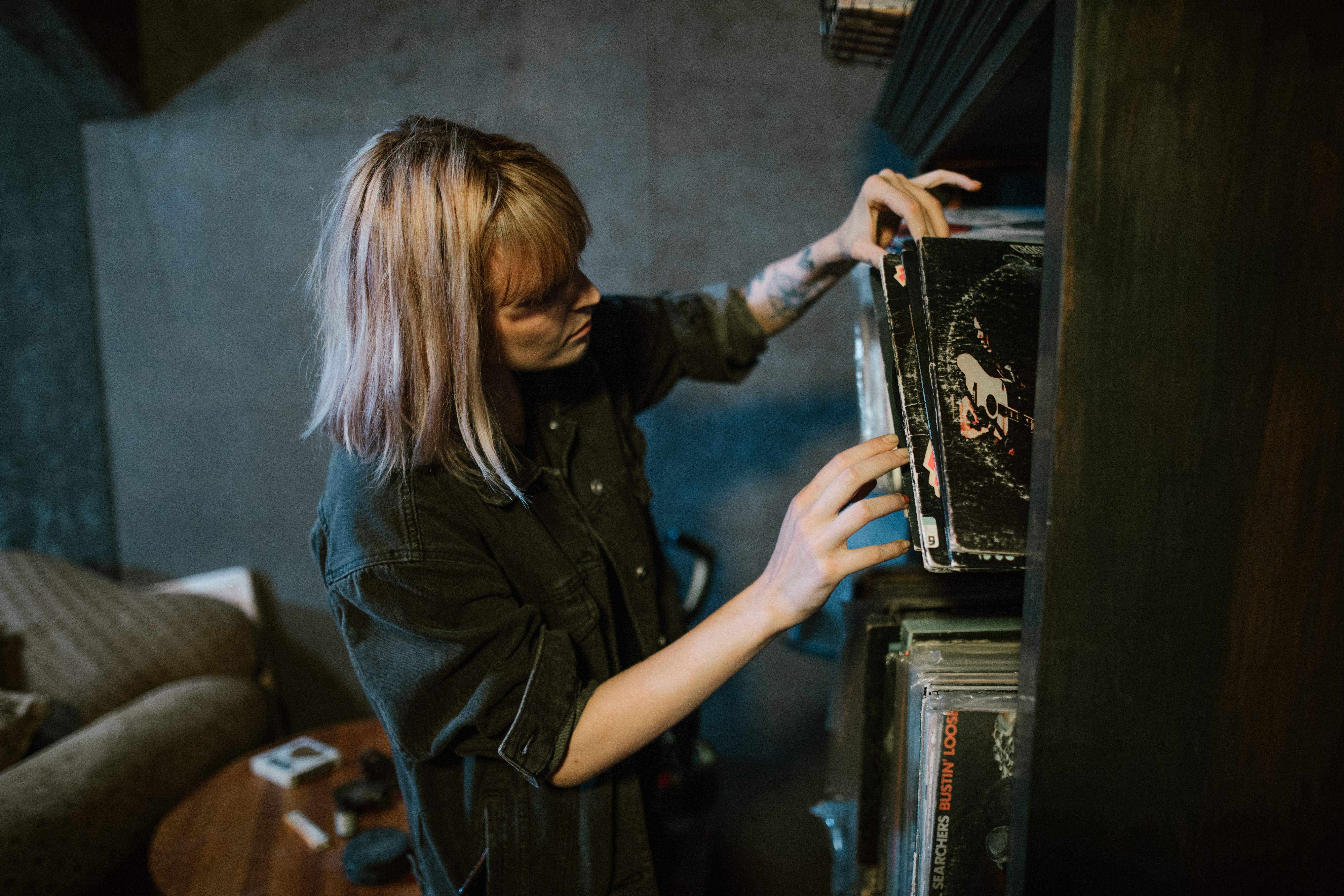 A woman in a black shirt explores a collection of vintage vinyl records on a wooden shelf indoors.