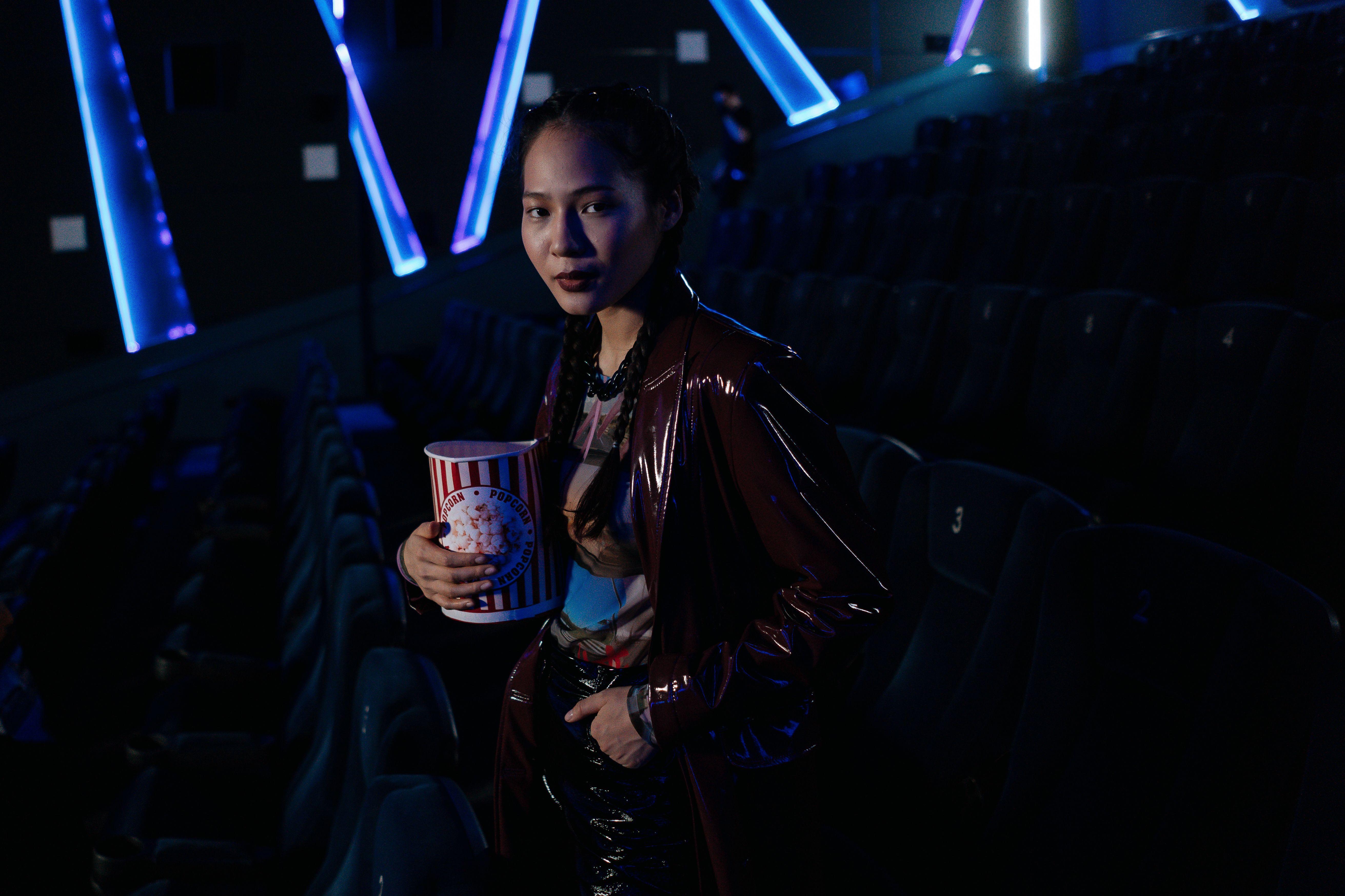 A stylish young woman holding popcorn in a dimly lit cinema, ready for a movie night experience.