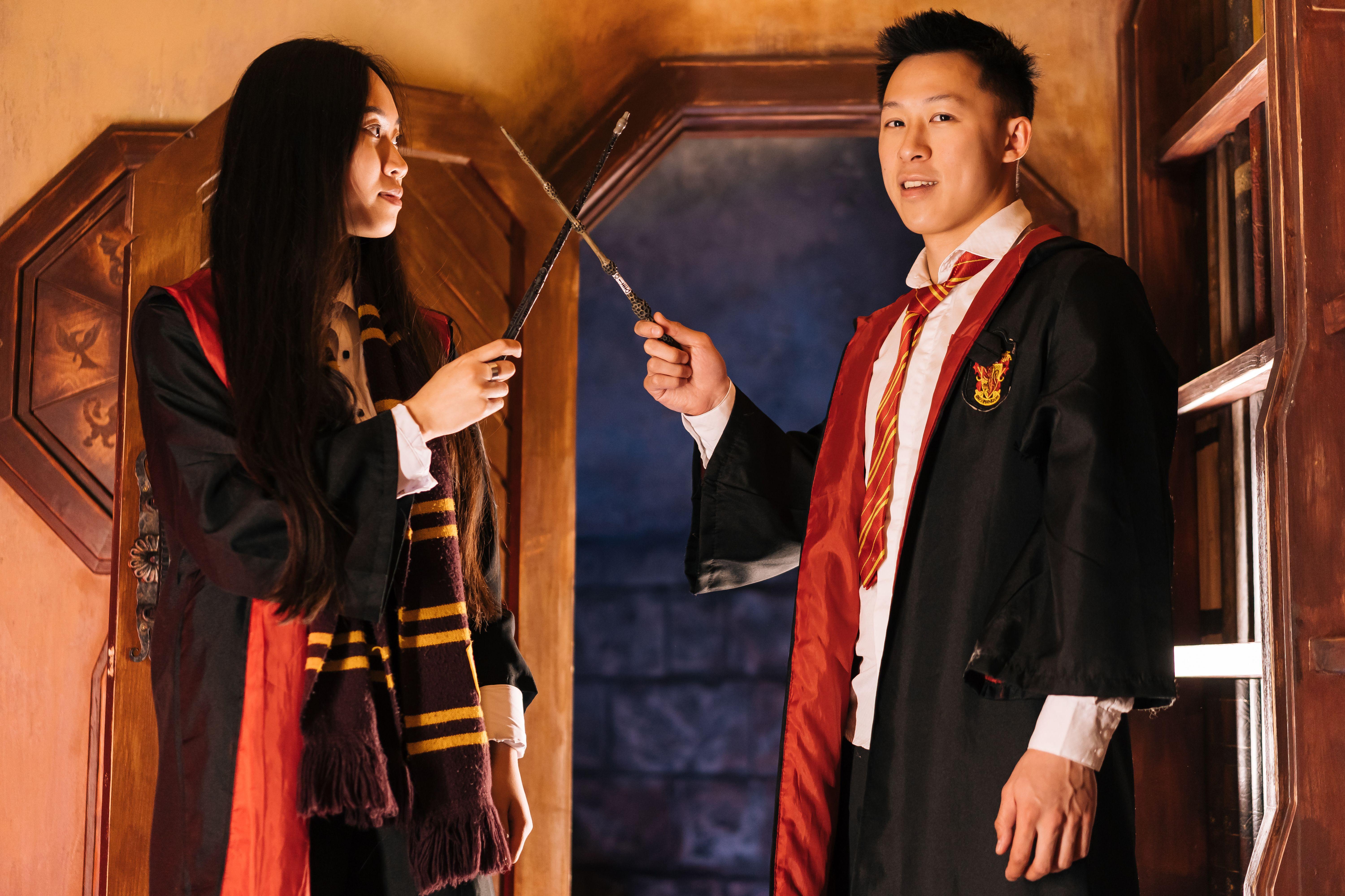 Two young adults dressed as wizards holding wands in a magical setting.