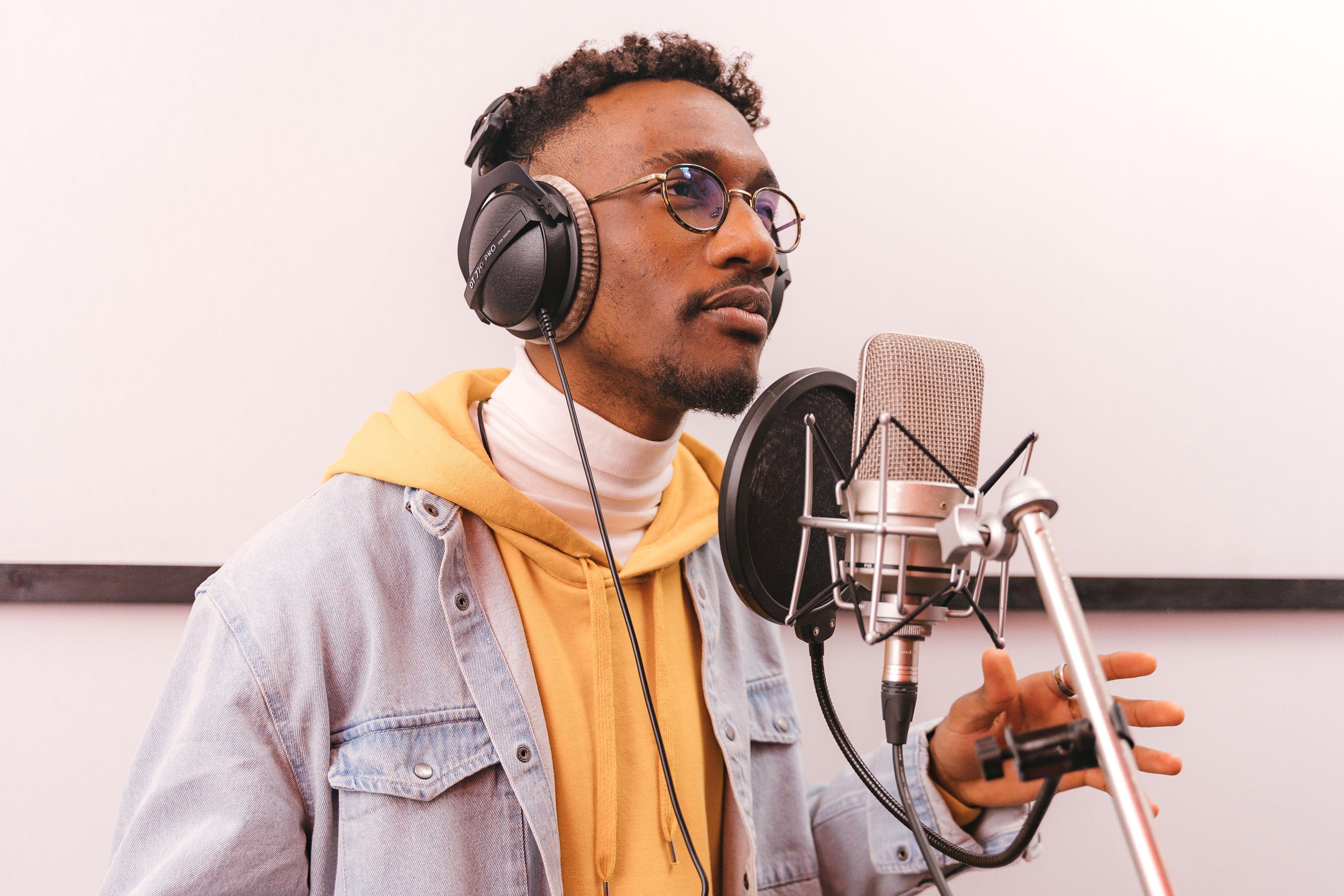 Casual African American man recording music with microphone in professional studio.