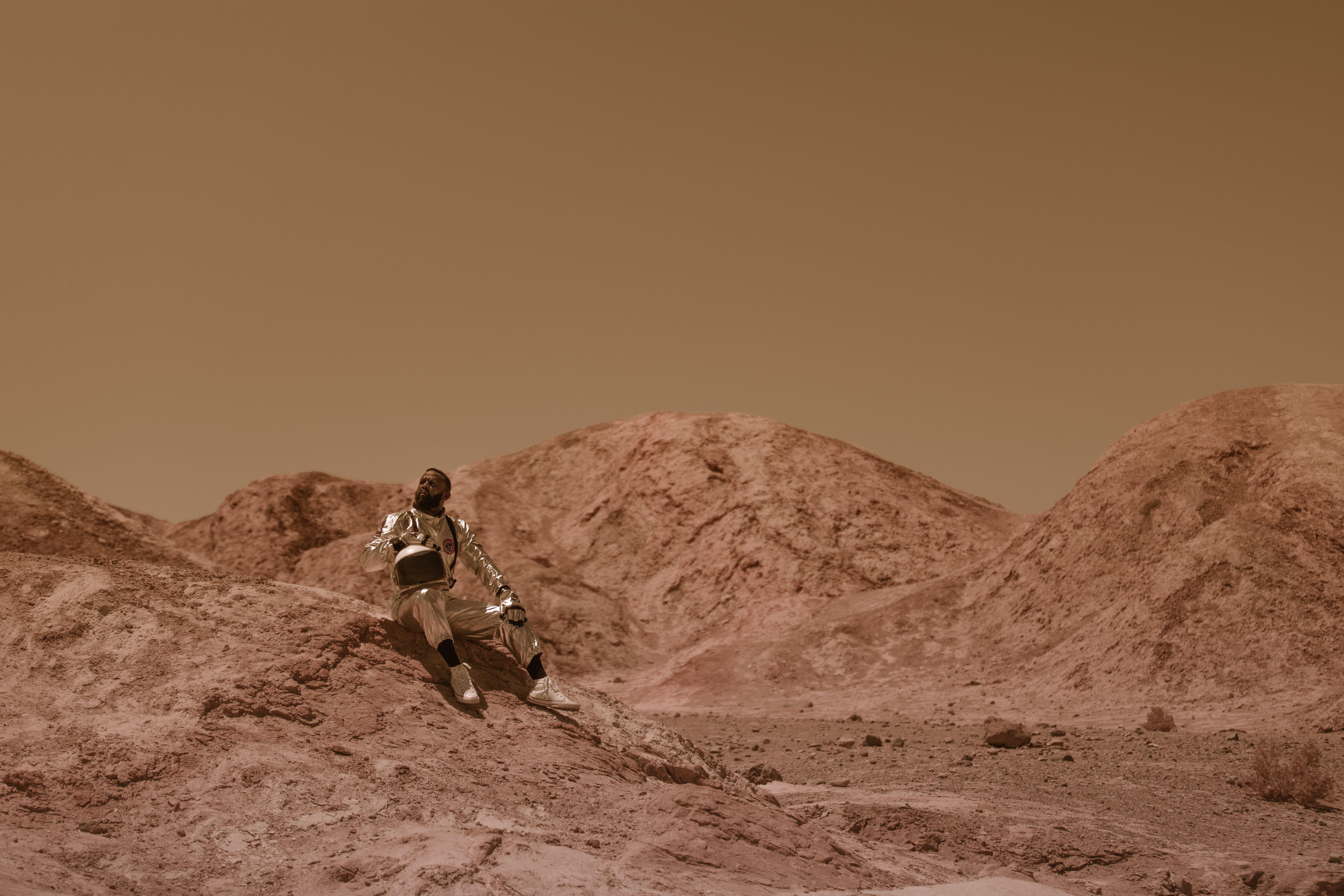 Astronaut in space suit sits on rocky desert terrain, evoking alien exploration.