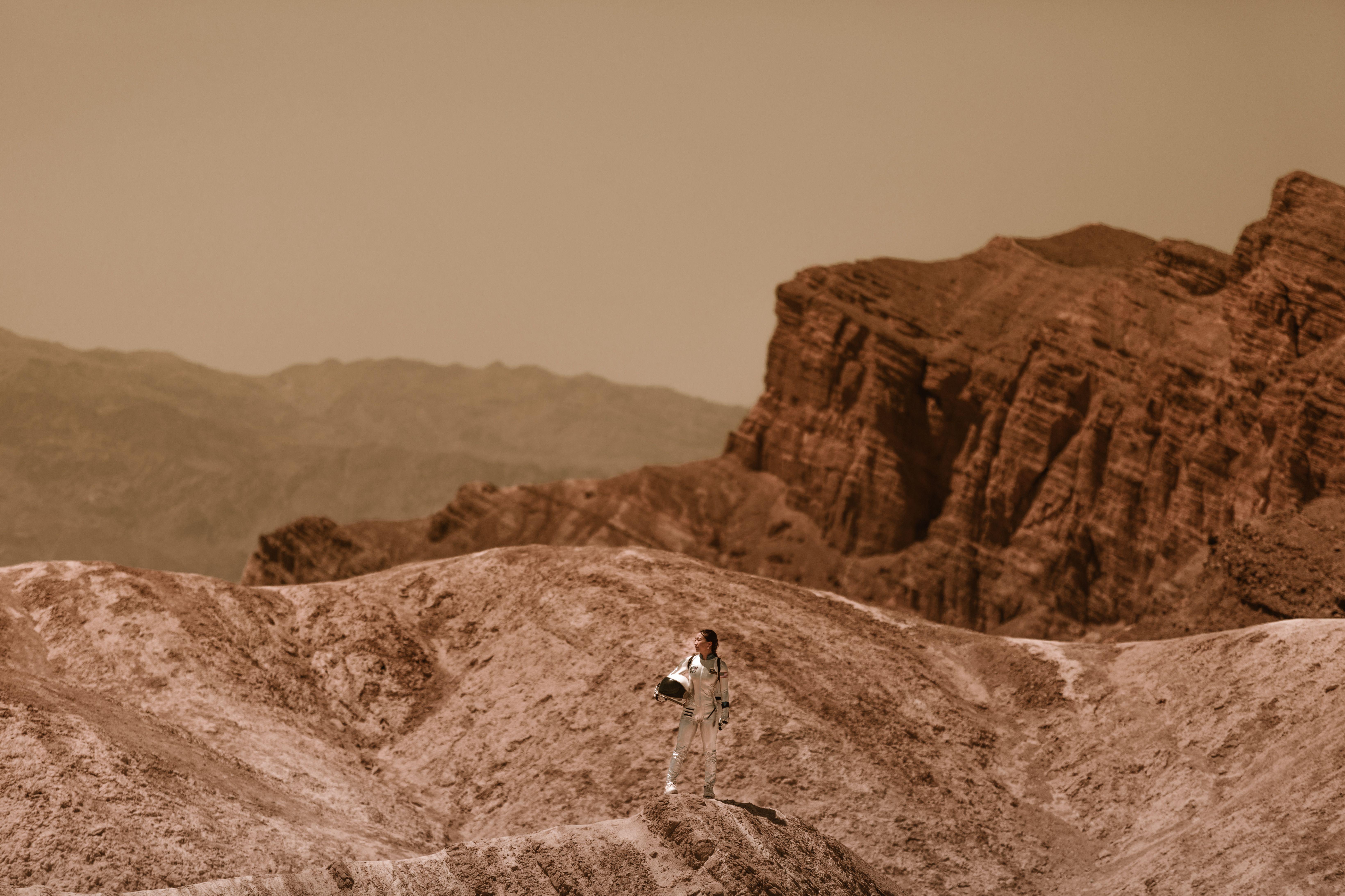 A woman astronaut stands on a barren, alien terrain, symbolizing space colonization.