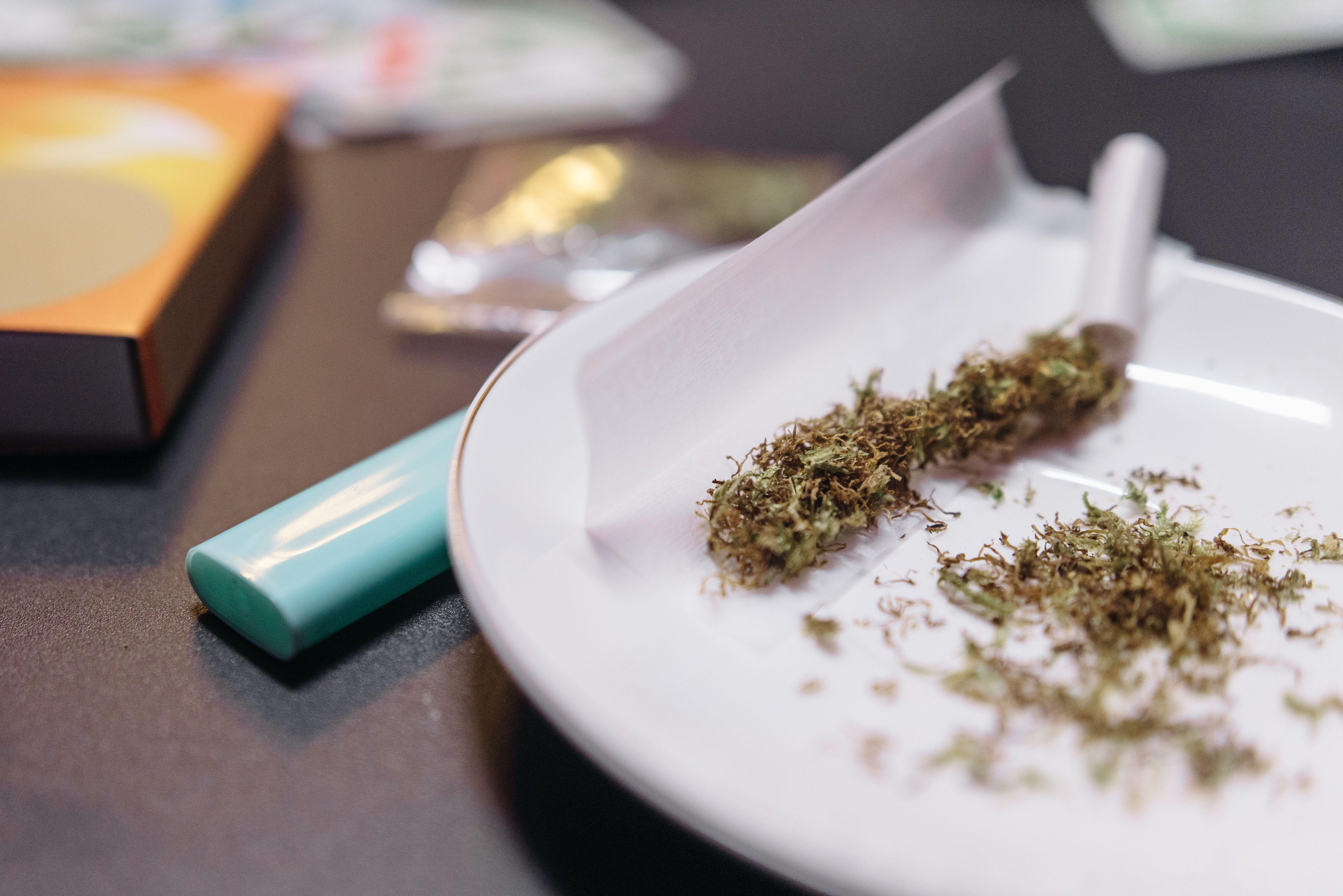 A close-up view of cannabis being prepared for rolling with a lighter and ceramic plate.