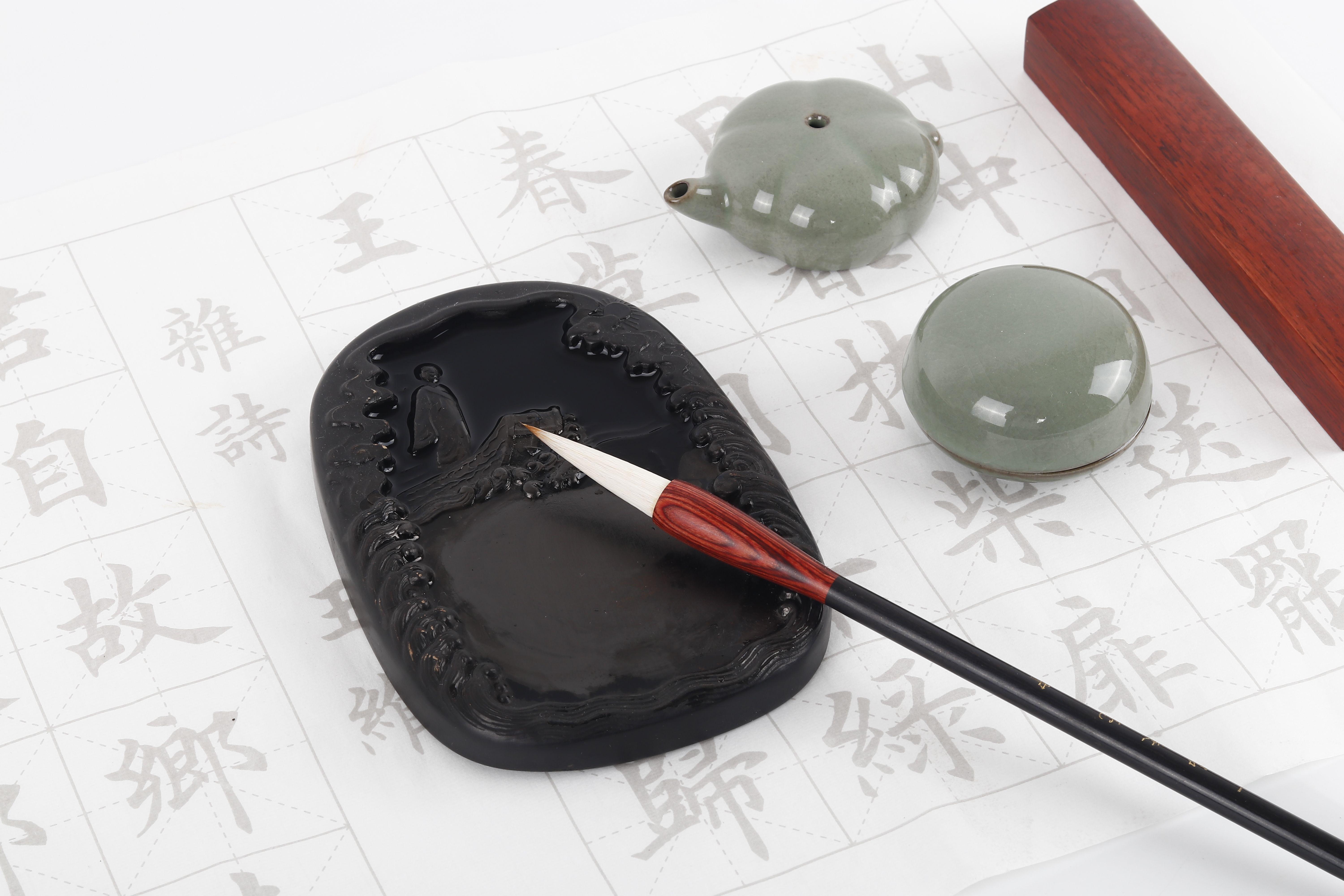 Flat lay of a traditional calligraphy set with ink stone, brush, and worksheet showcasing Chinese characters.