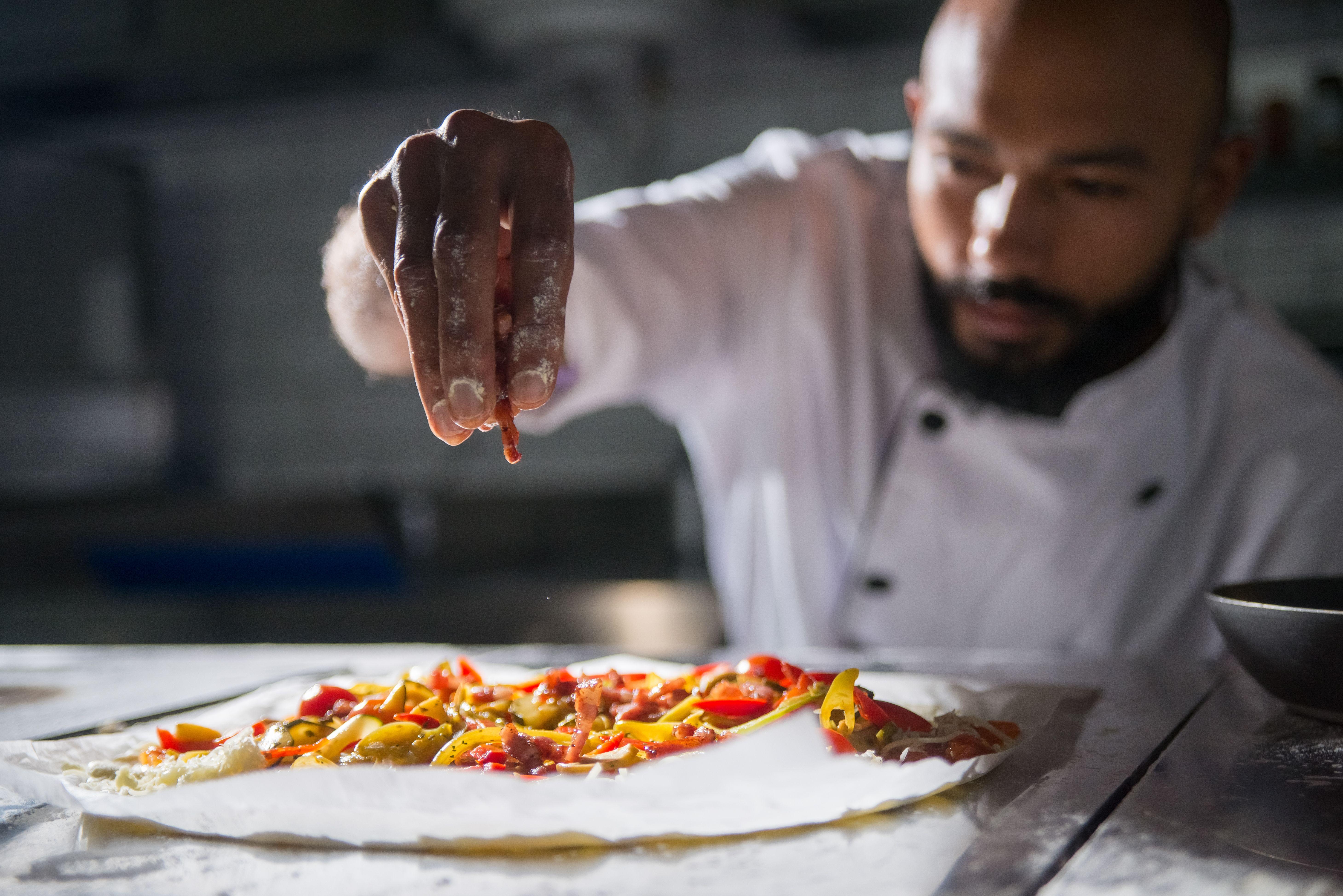 Professional chef skillfully preparing a vibrant homemade pizza with fresh ingredients.
