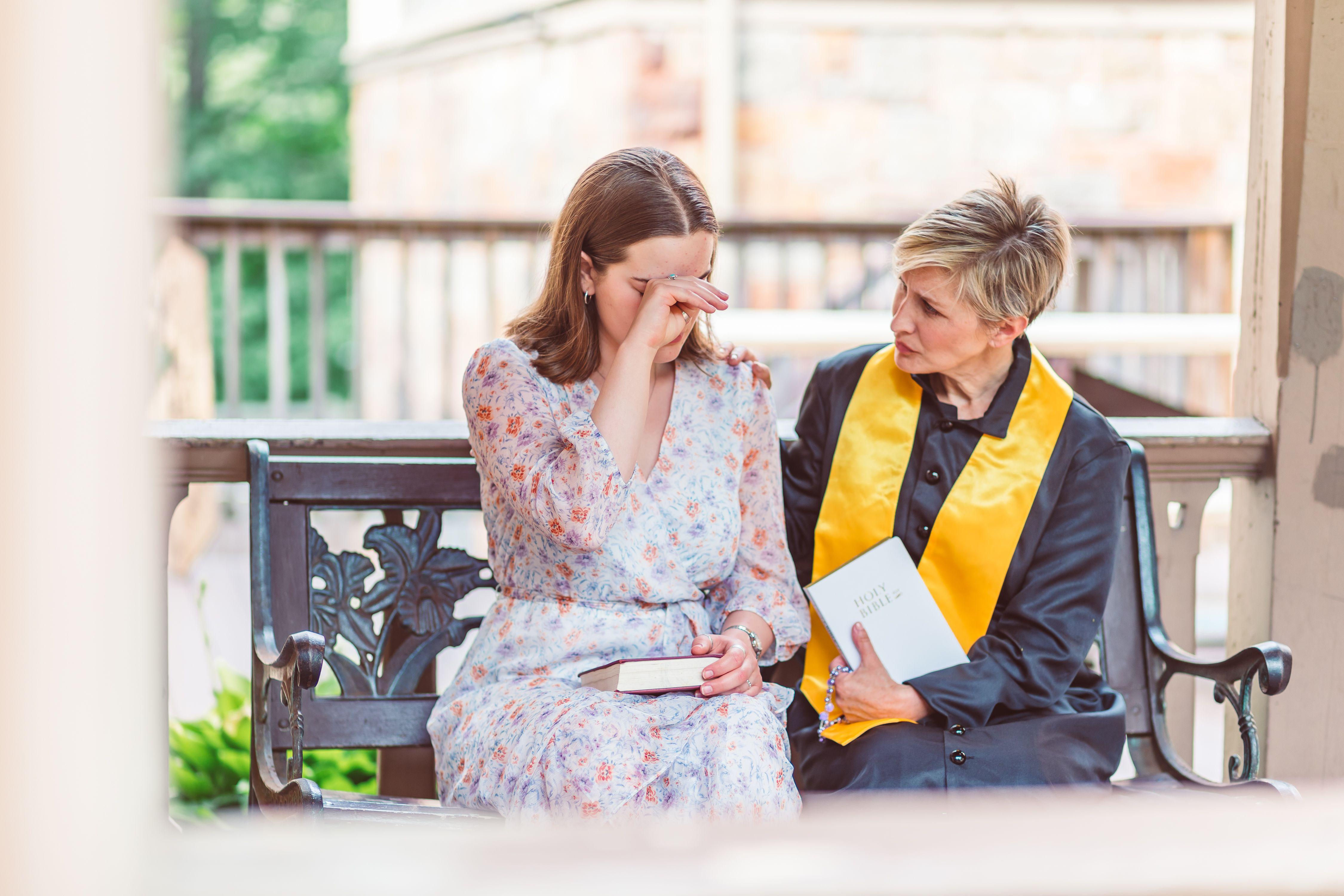 Woman receiving emotional support from a priest on a church bench.