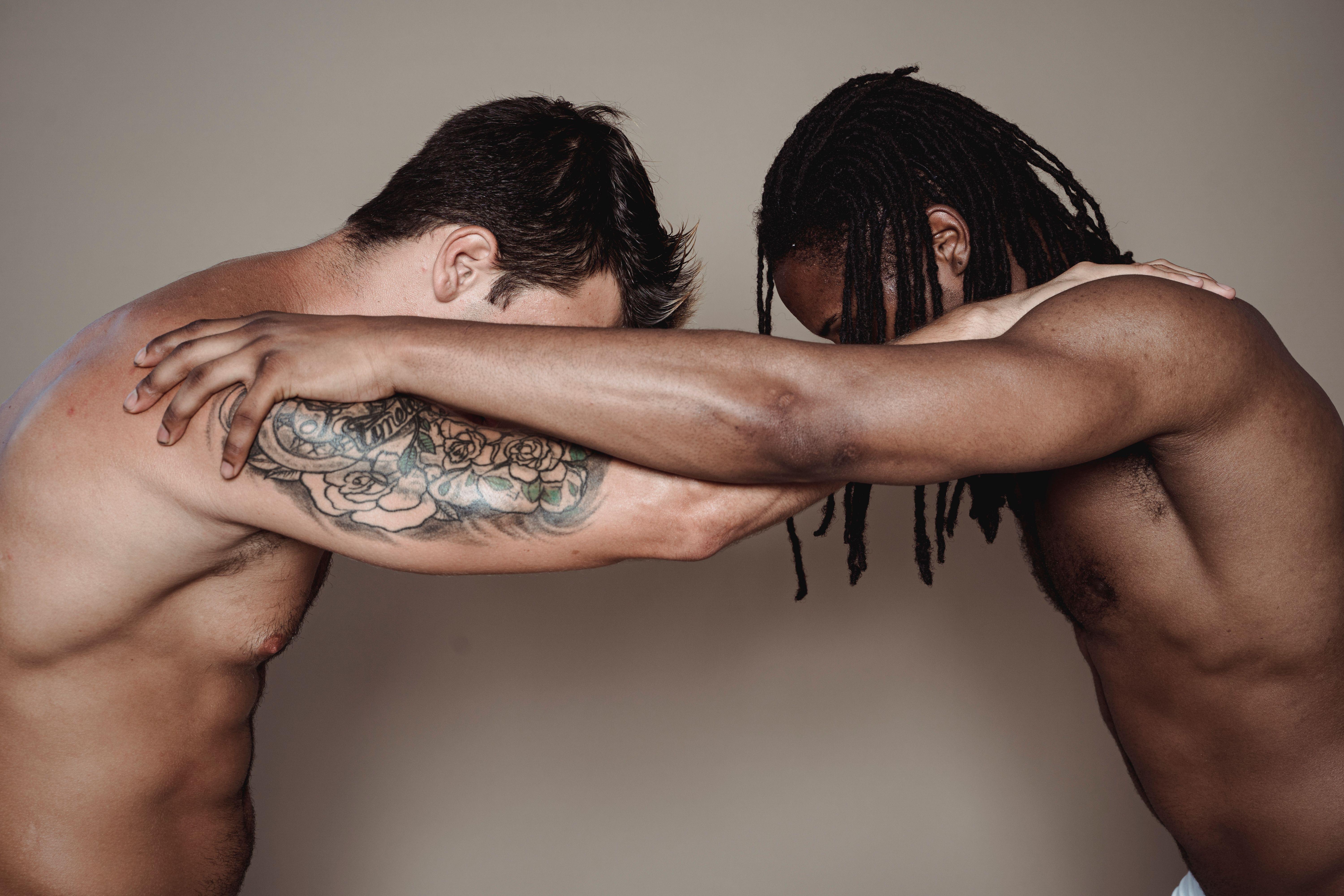 Two muscular men with intertwined arms in a studio setting, showing strength and diversity.