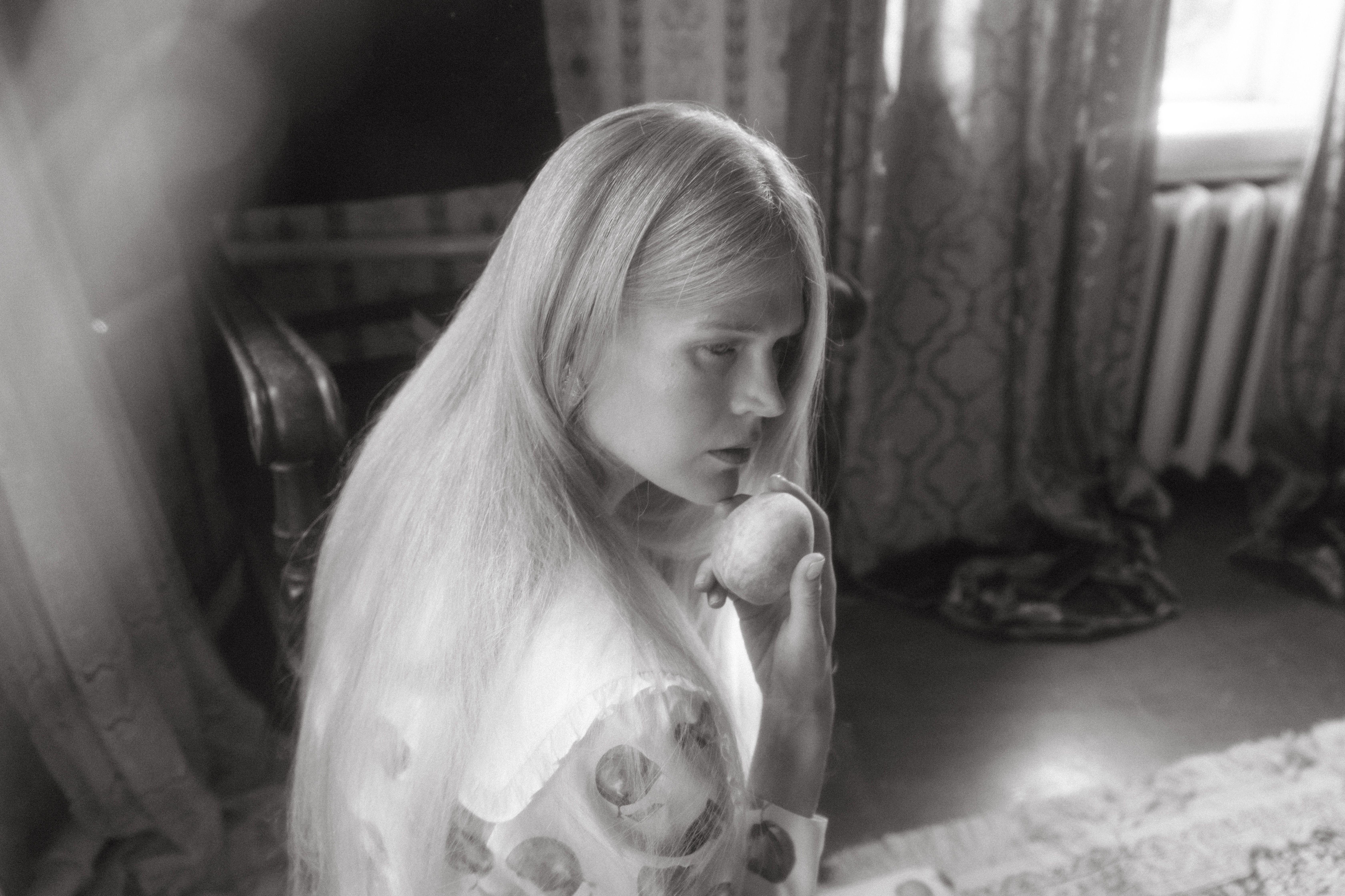 A vintage-style grayscale photo depicting a woman with long hair holding a fruit indoors.