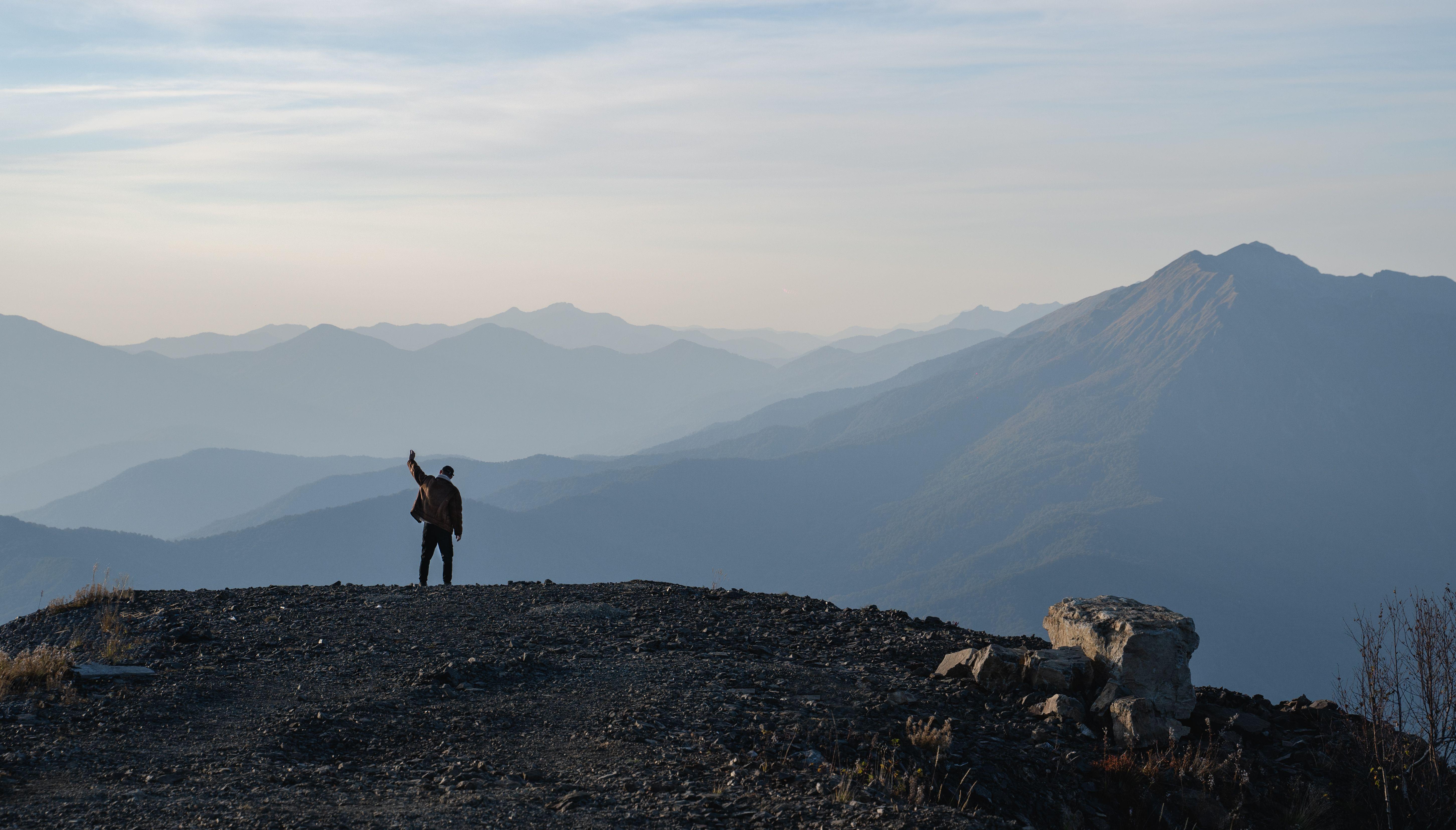 Silhouette of a person celebrating on a mountain summit at twilight with panoramic views.