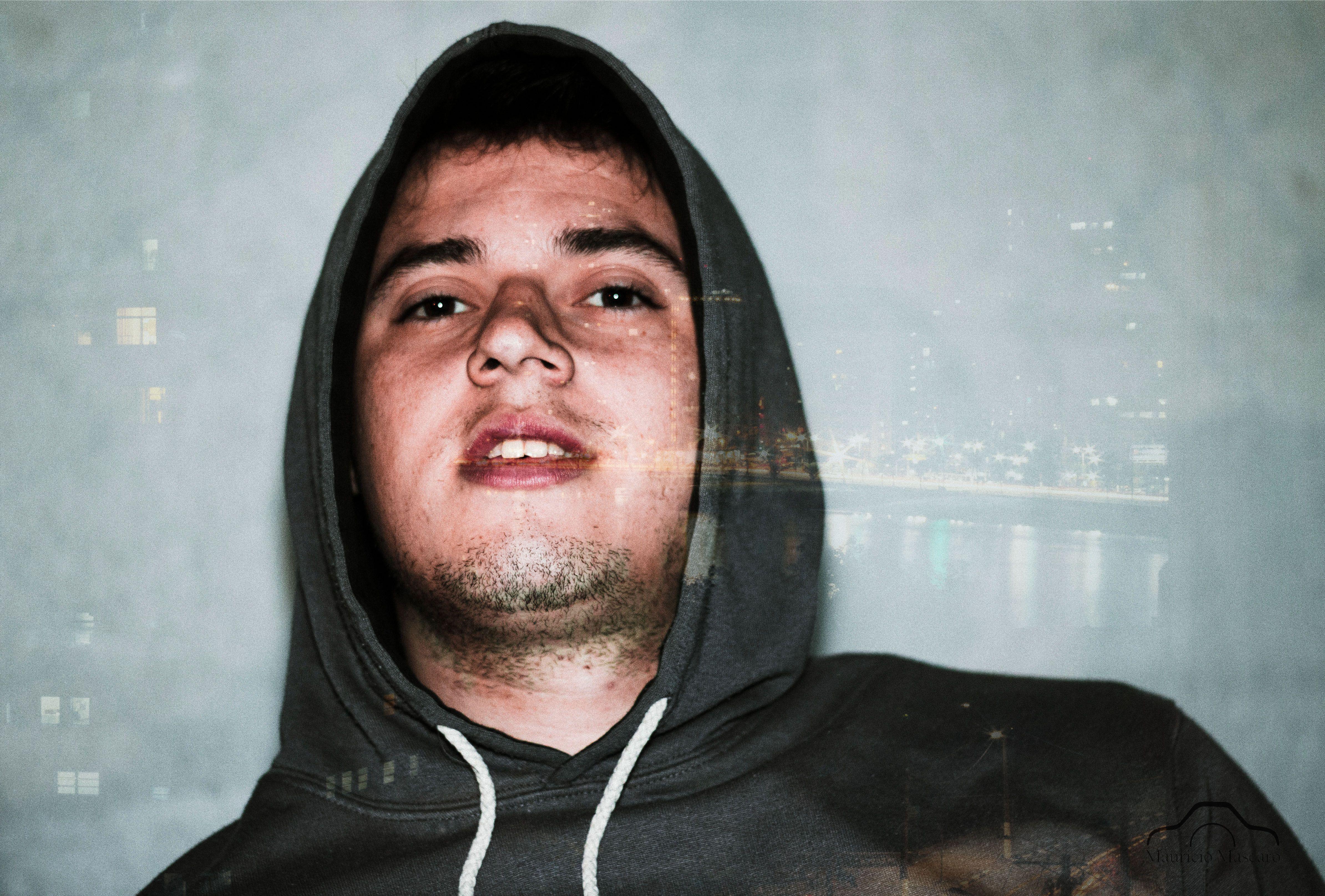 A creative double exposure portrait of a young man in a hoodie with city lights overlay.