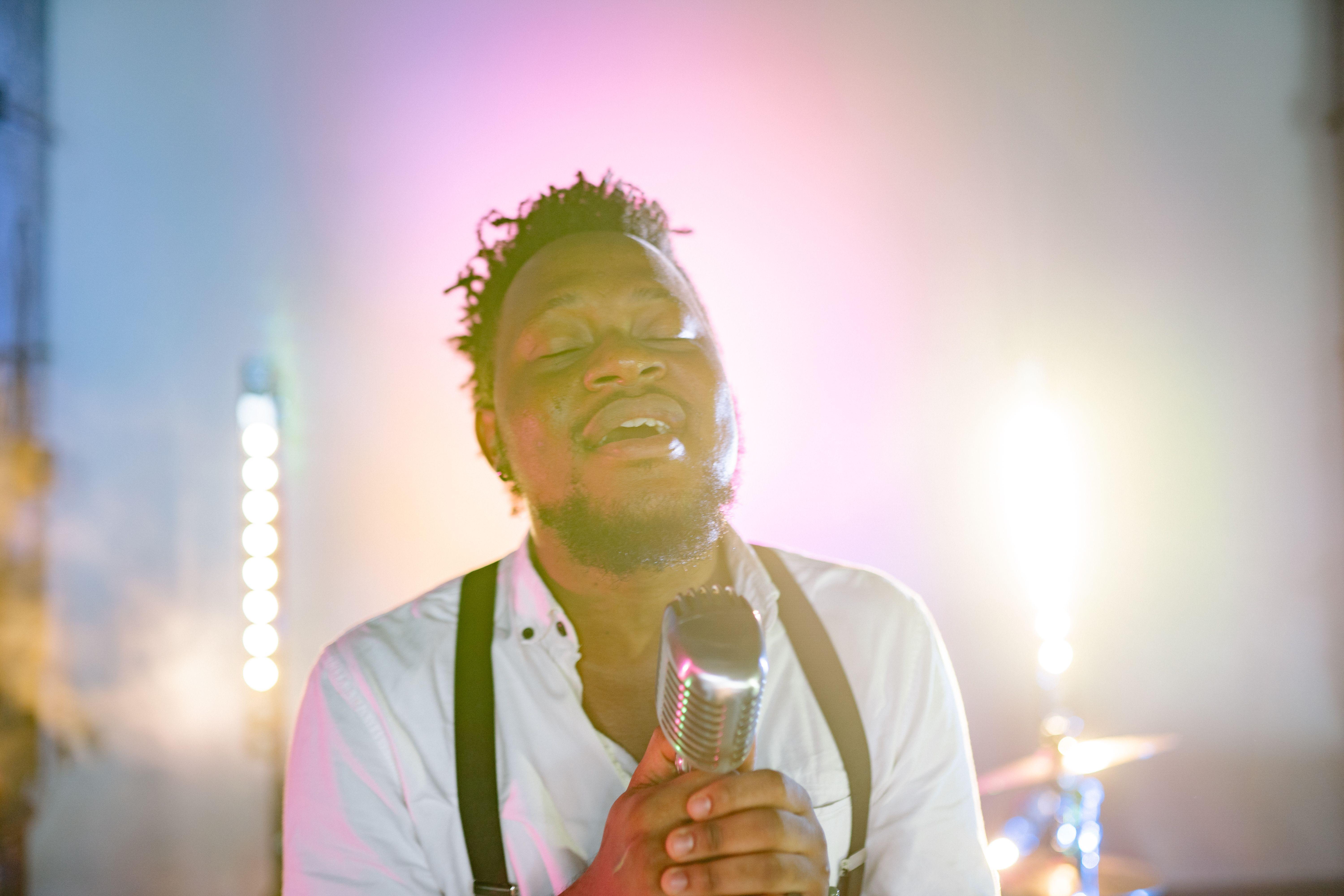 An African American man passionately singing into a retro microphone on stage.