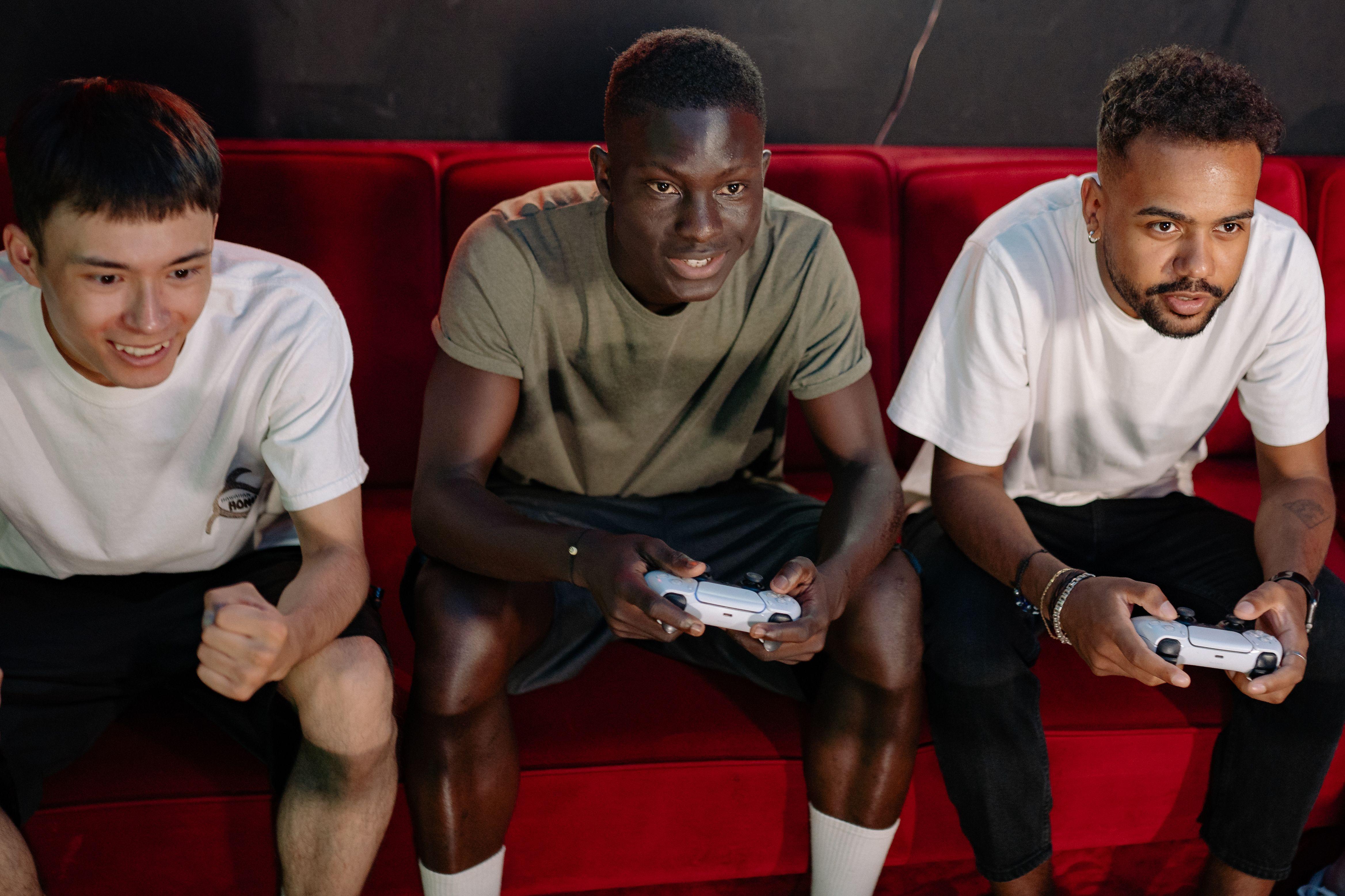 Three young men gaming on a sofa, showcasing diversity and fun.