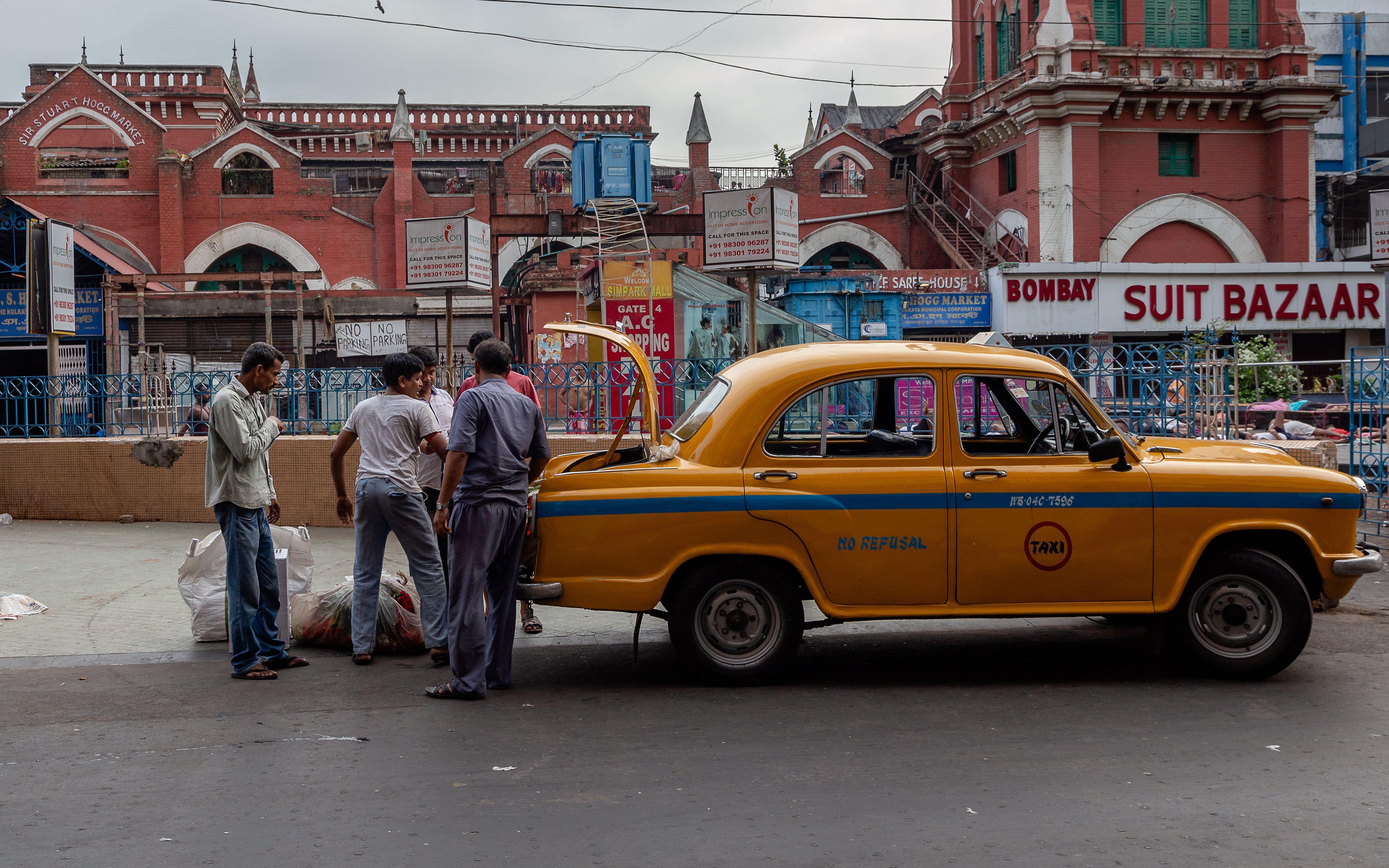 Street scene with a classic yellow taxi and people on a bustling city road.
