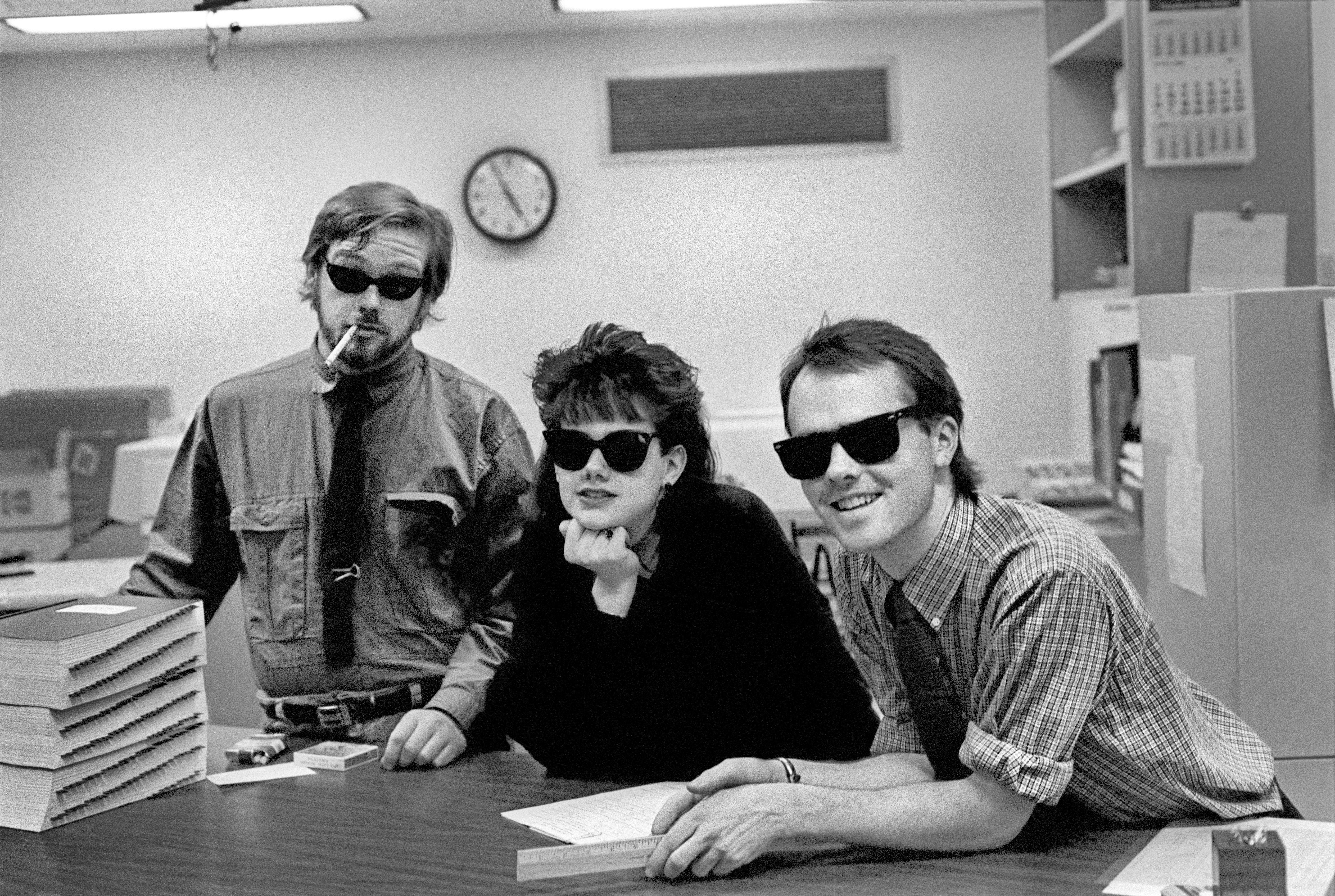 Black and white photo of three coworkers in an office wearing sunglasses, displaying a playful vibe.