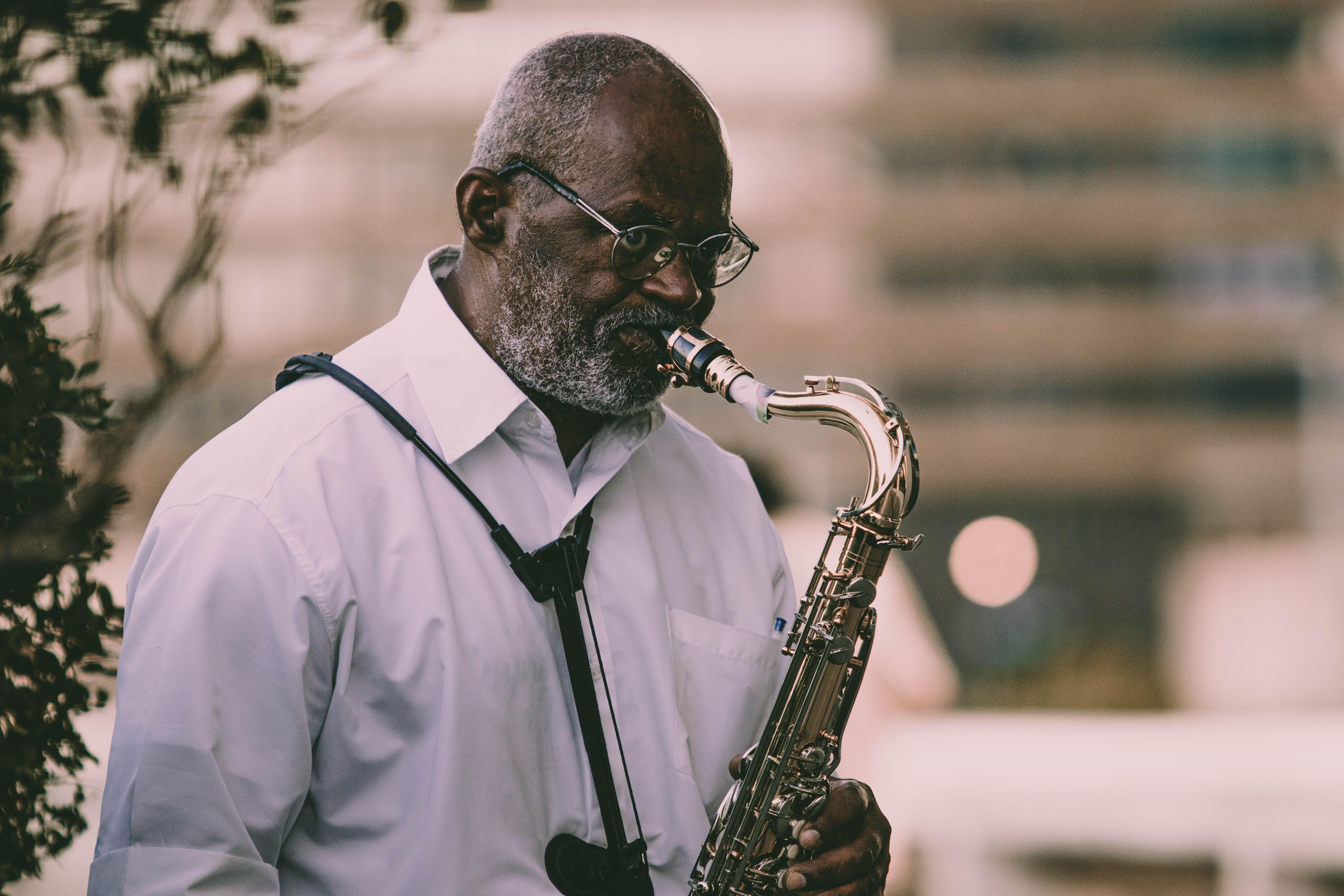 An elderly musician playing a saxophone outdoors in a serene setting.