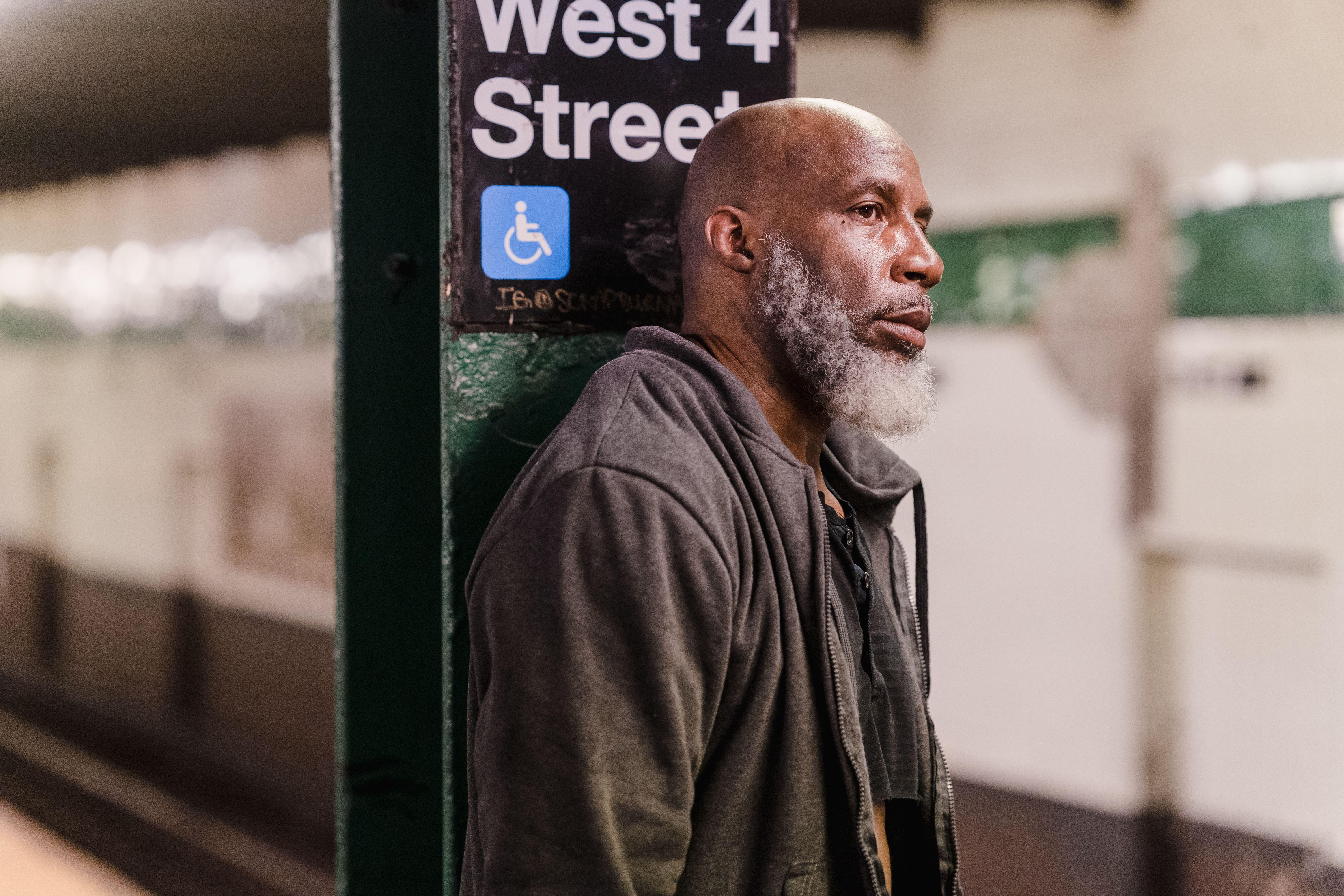 Elderly man standing thoughtfully at West 4th Street subway platform, conveying urban solitude.