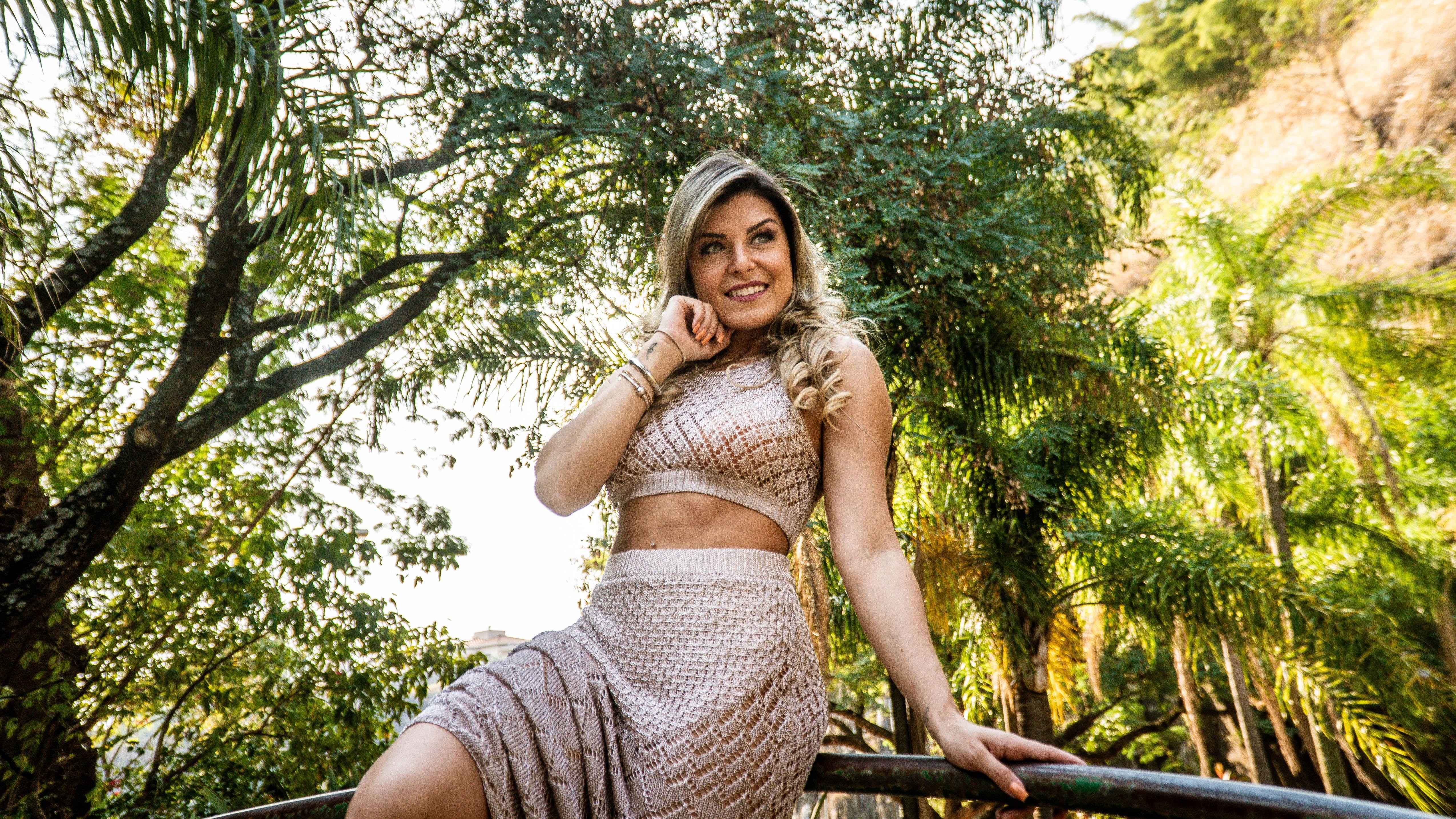 Stylish woman in a crop top smiling amidst lush greenery on a sunny day.