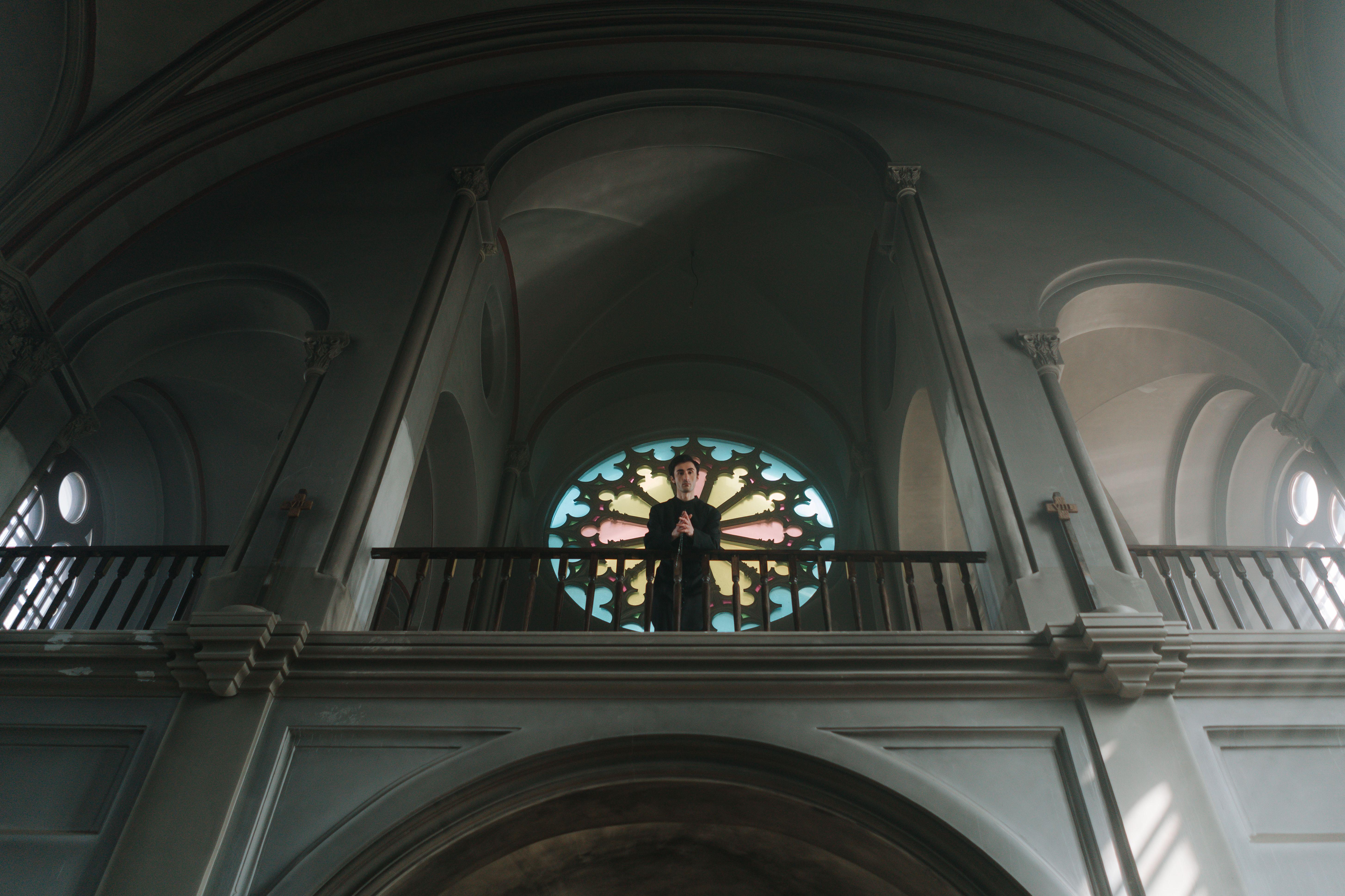 A priest stands at the altar in an ornate church with beautiful arches and stained glass.