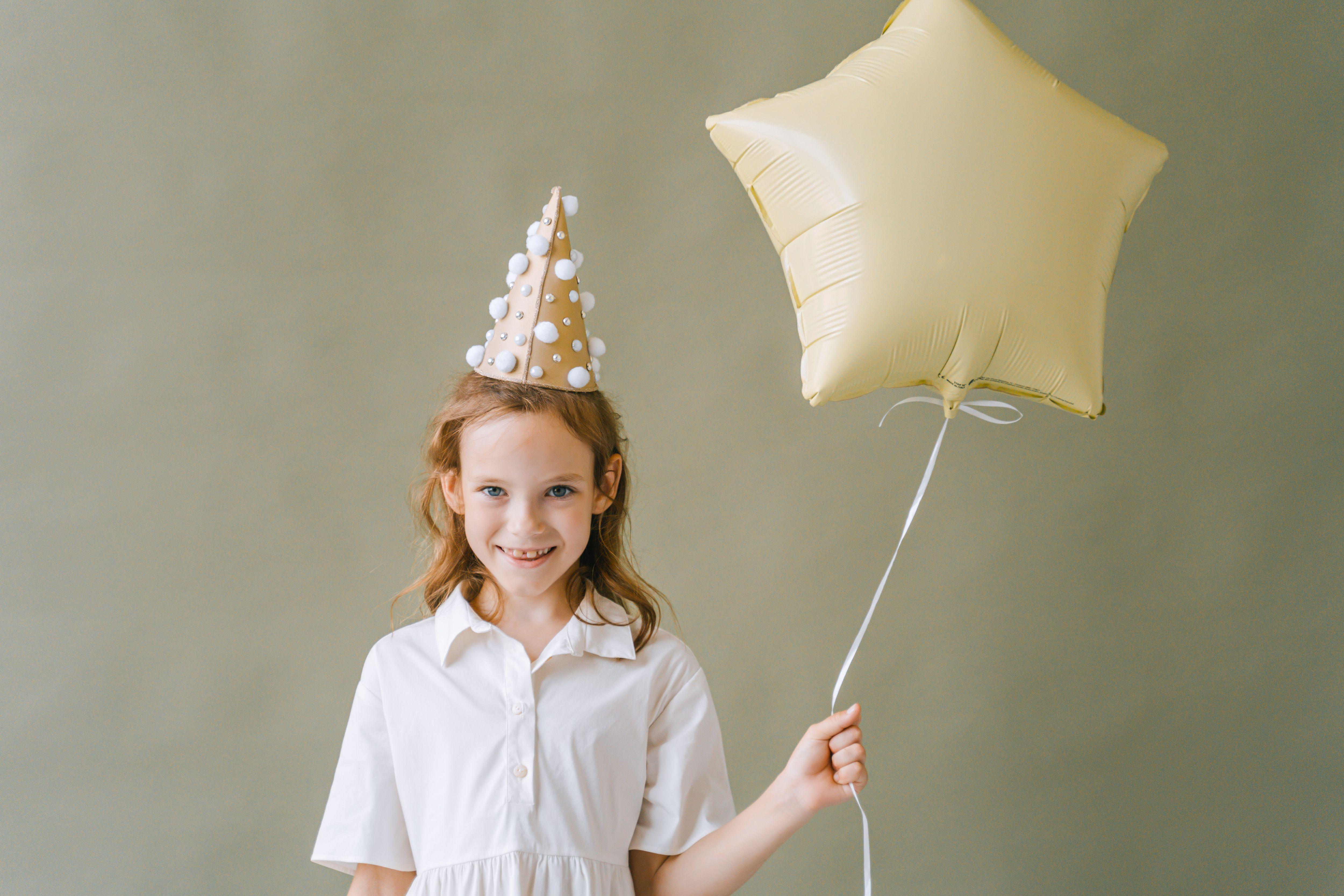 Smiling girl with party hat and star balloon, enjoying a fun birthday celebration.