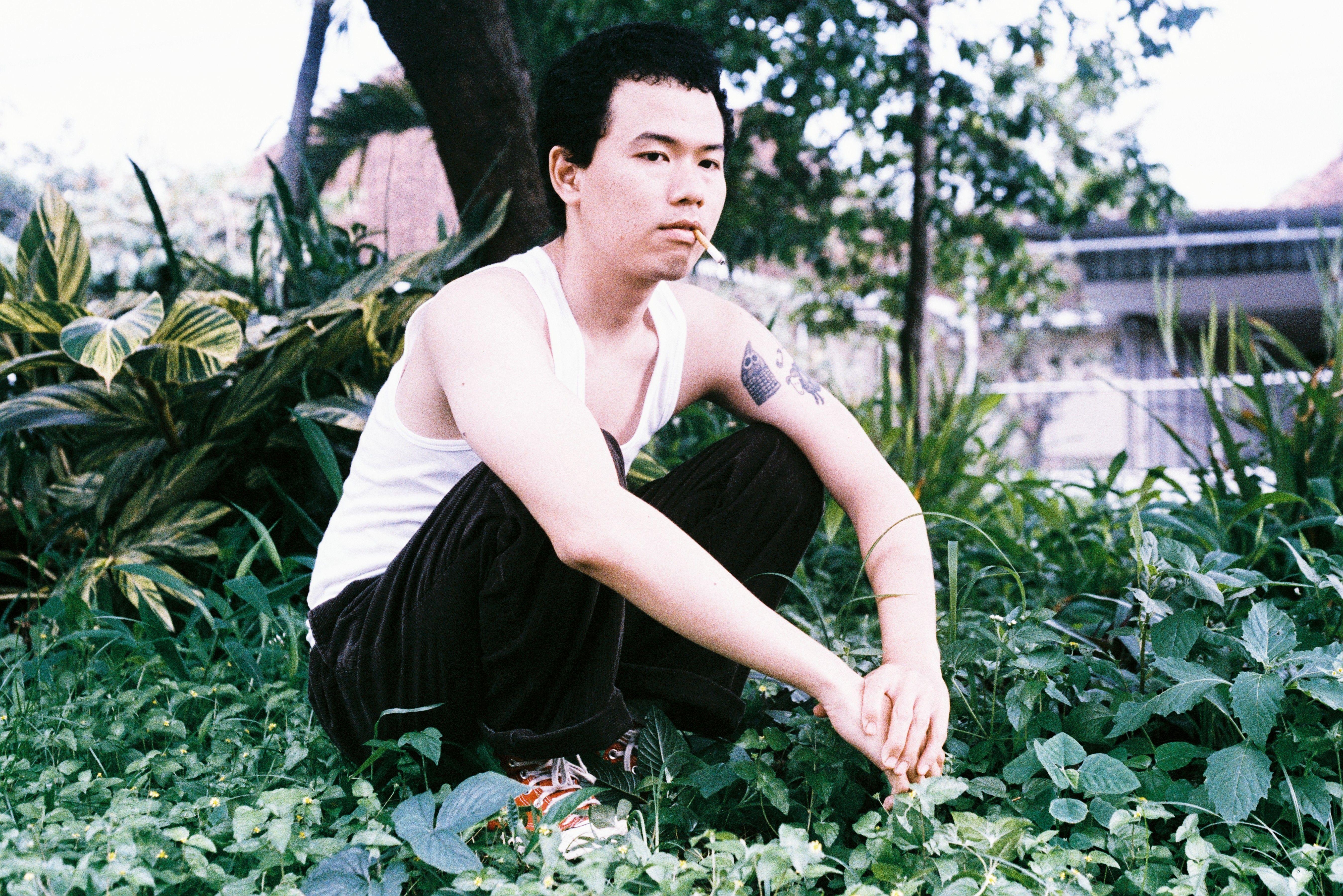 A young man in a garden, crouching with a cigarette, conveys a relaxed lifestyle vibe.