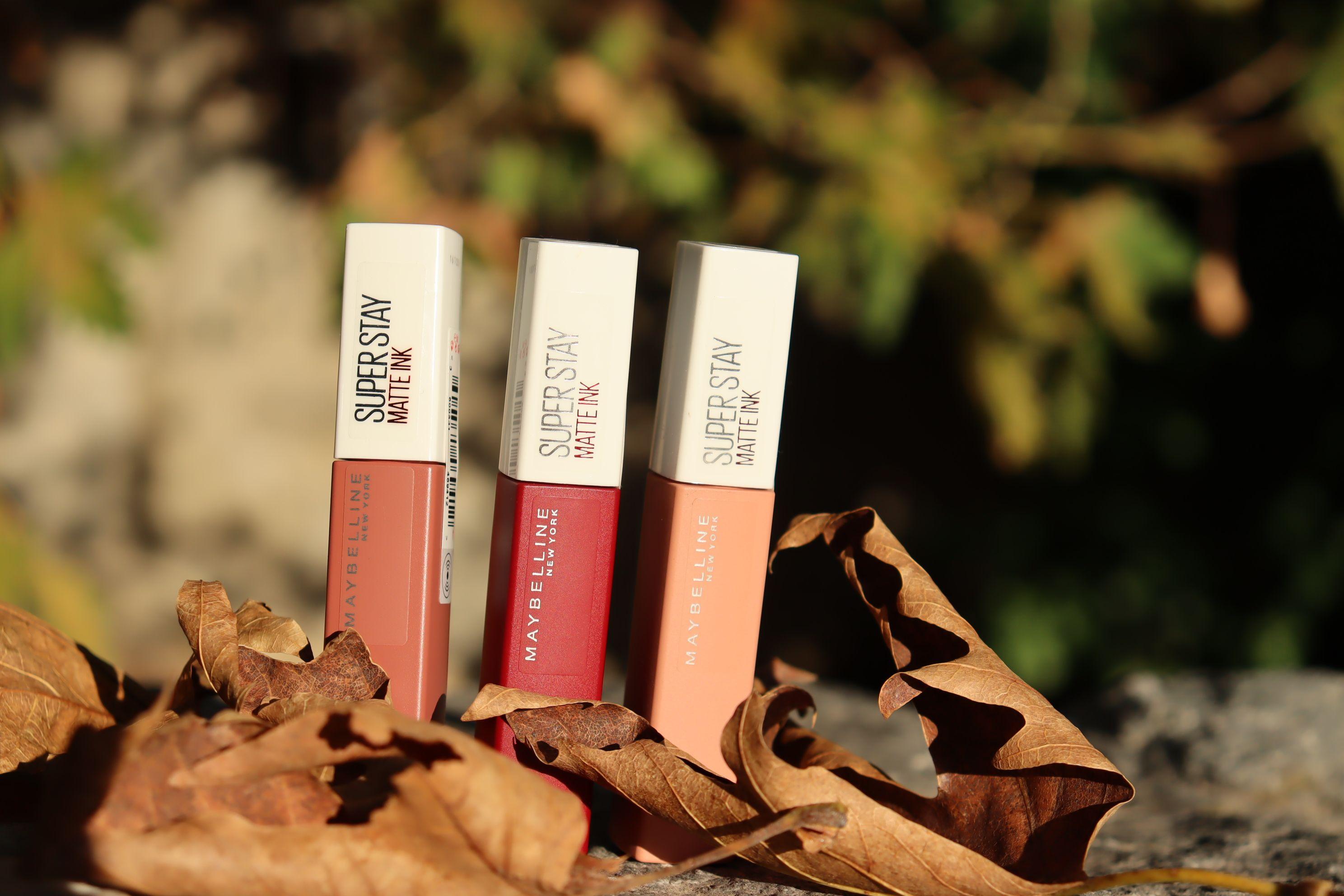 Three Maybelline Super Stay Matte Ink lipsticks among fall leaves, highlighting beauty essentials.